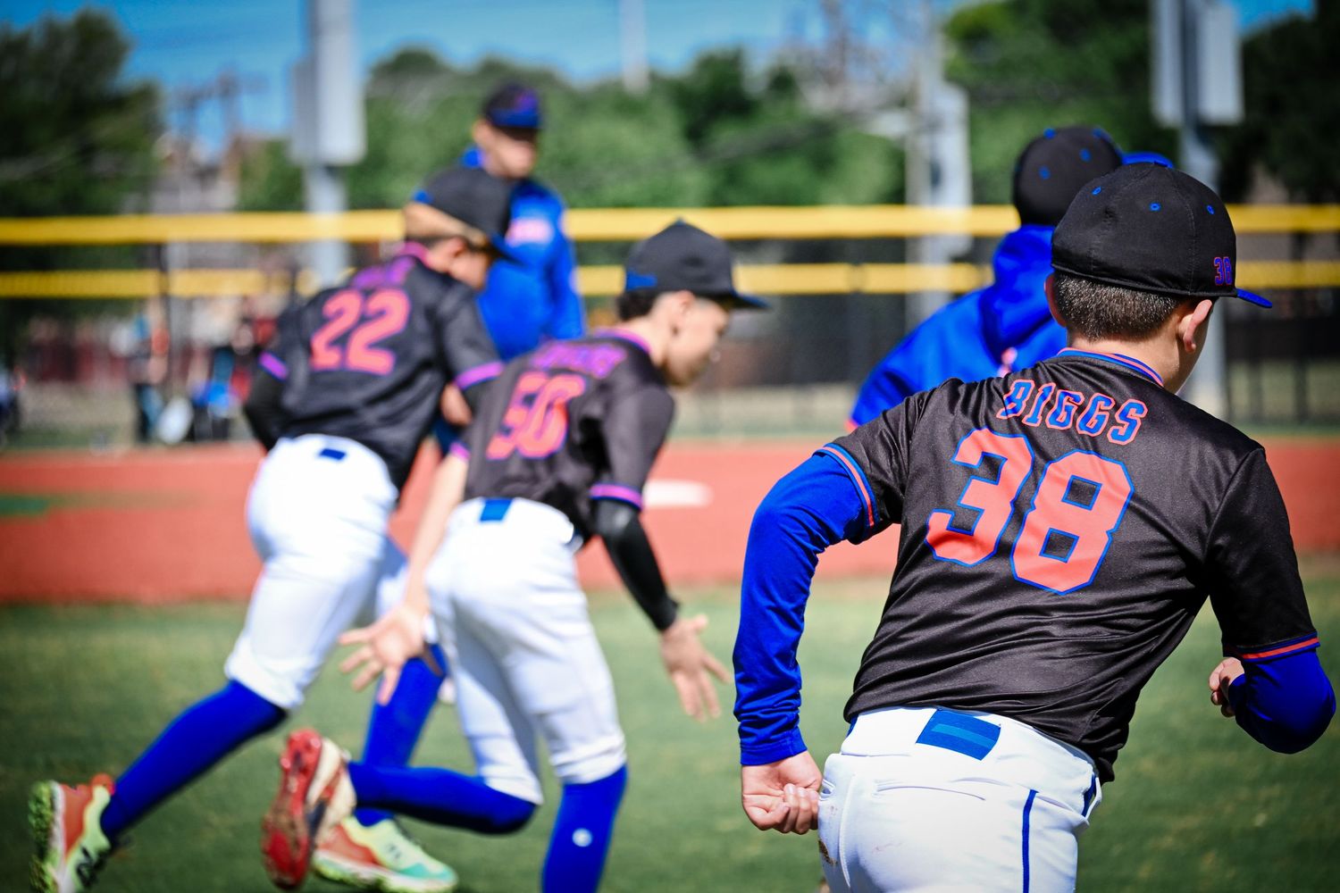 Youth baseball players in black and blue Mets uniforms warming up with stretches on field.