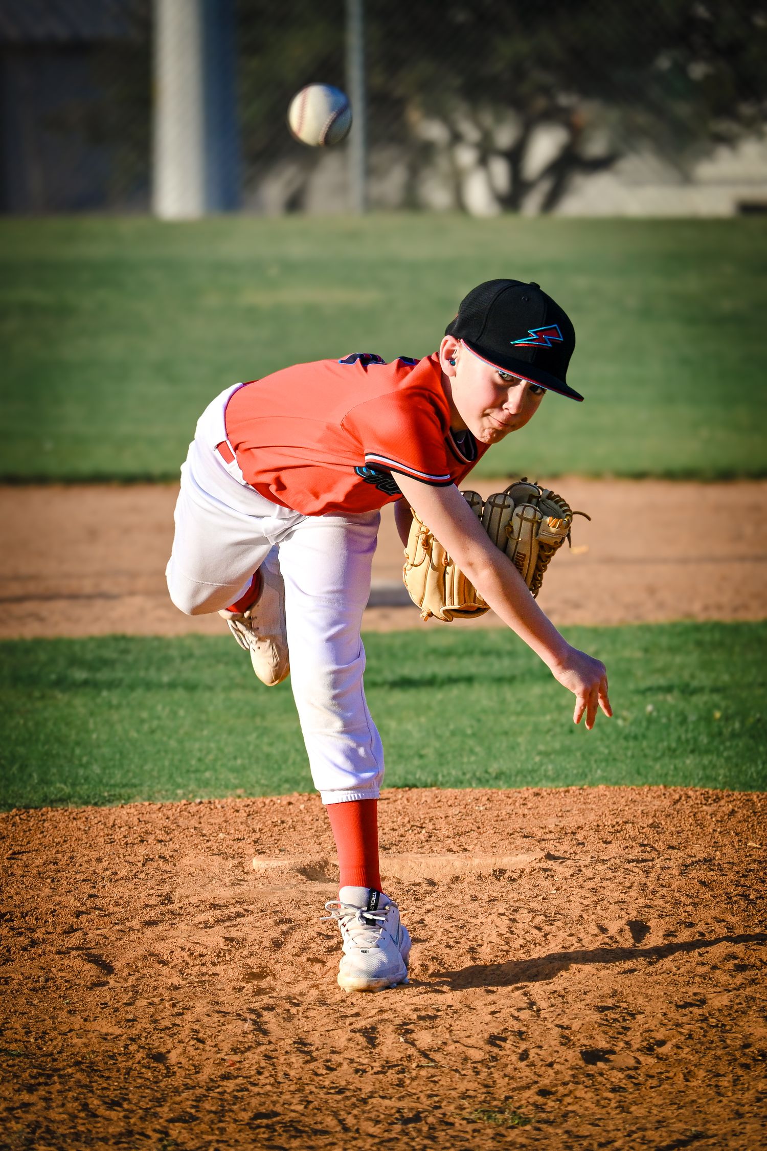 Young baseball pitcher in red uniform delivers pitch from mound during outdoor game.