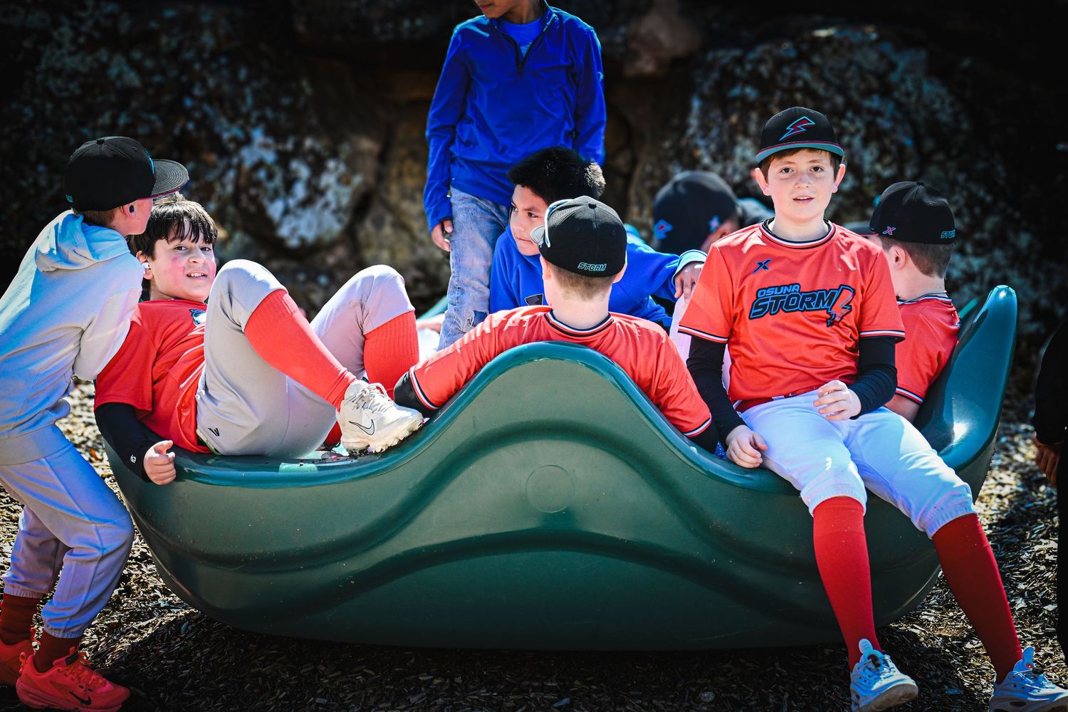 Youth baseball players in red and blue uniforms relax together on playground equipment.