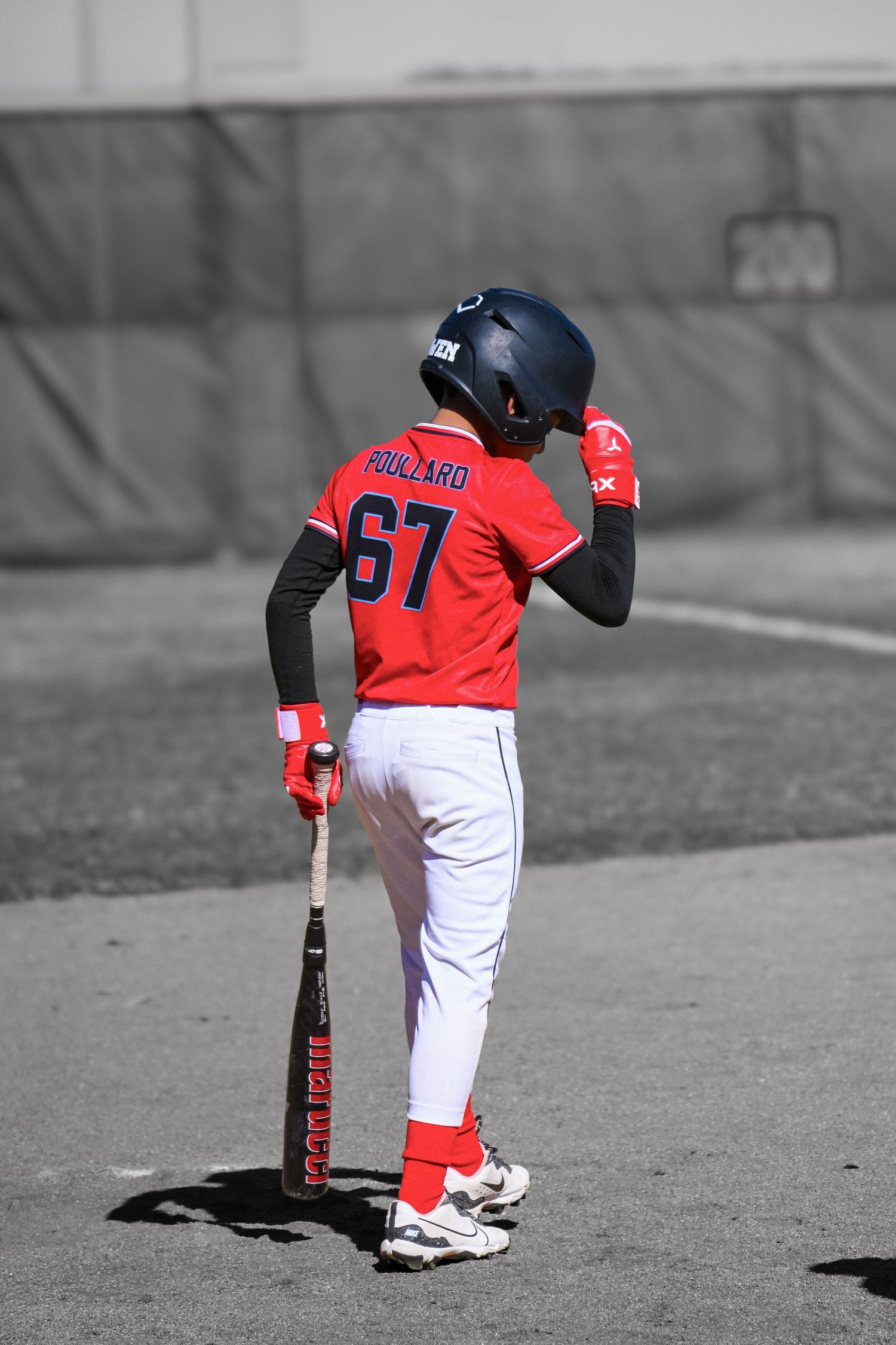 Youth baseball player number 67 Polizaro stands holding bat in red uniform and helmet.