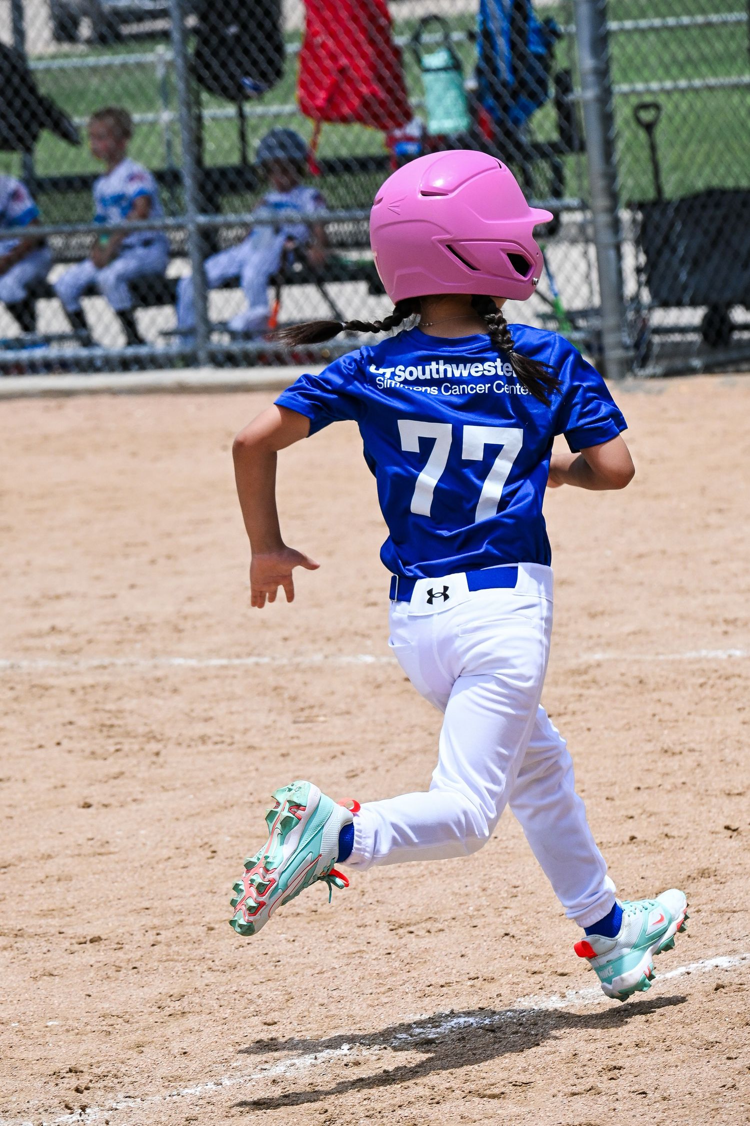 Young girl in pink helmet and number 77 blue jersey running bases during youth softball game.