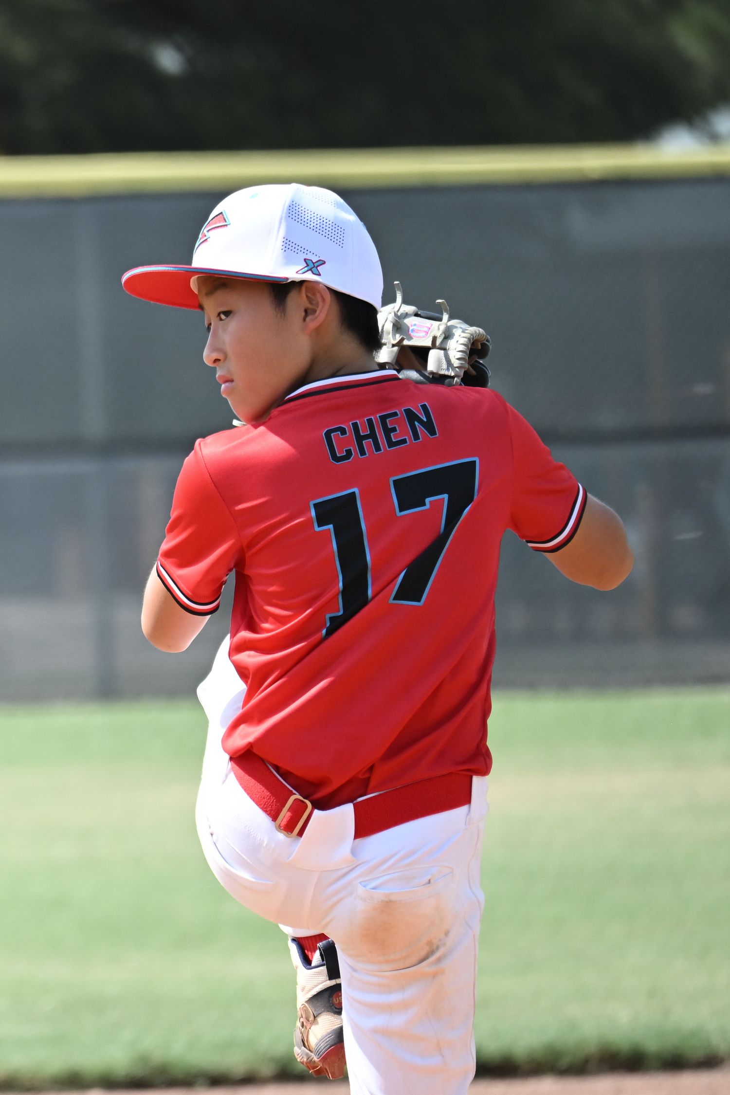 Young baseball pitcher #17 Chen winds up for a pitch in a red uniform during a youth baseball game.