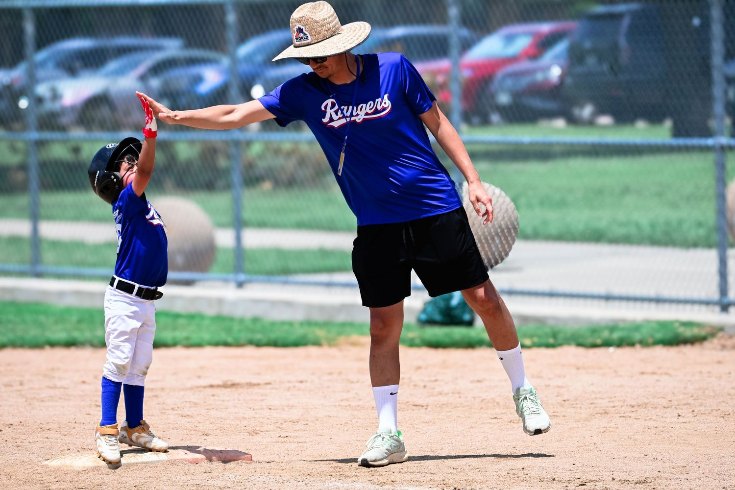 Little league baseball coach in Rangers jersey giving high five to young player on baseball field.