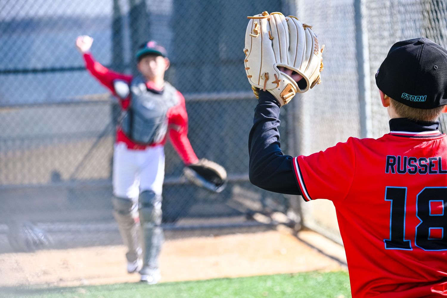 Youth baseball player wearing Russell 18 jersey holds glove up to catch a throw during bullpen practice.