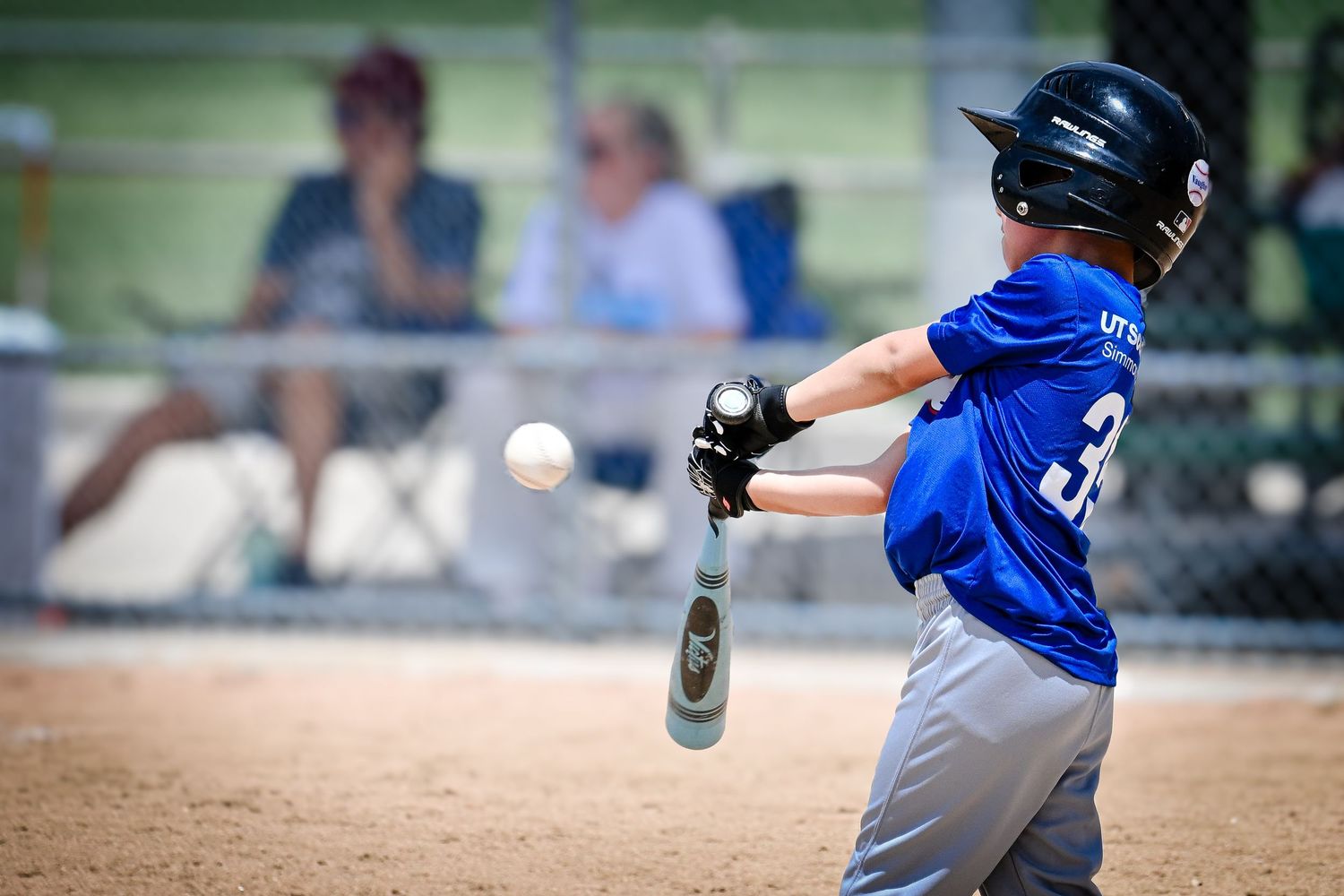 Young baseball player in blue uniform swinging bat at incoming pitch during youth league game outdoors.