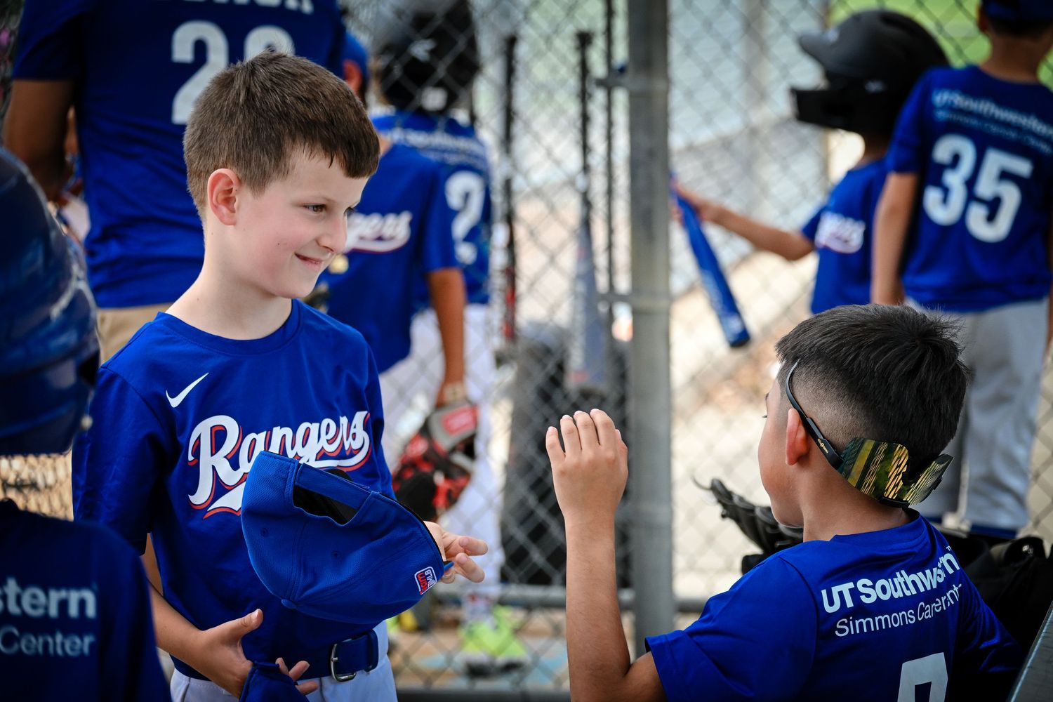 Two young boys in Rangers baseball uniforms giving high fives near dugout fence after game.