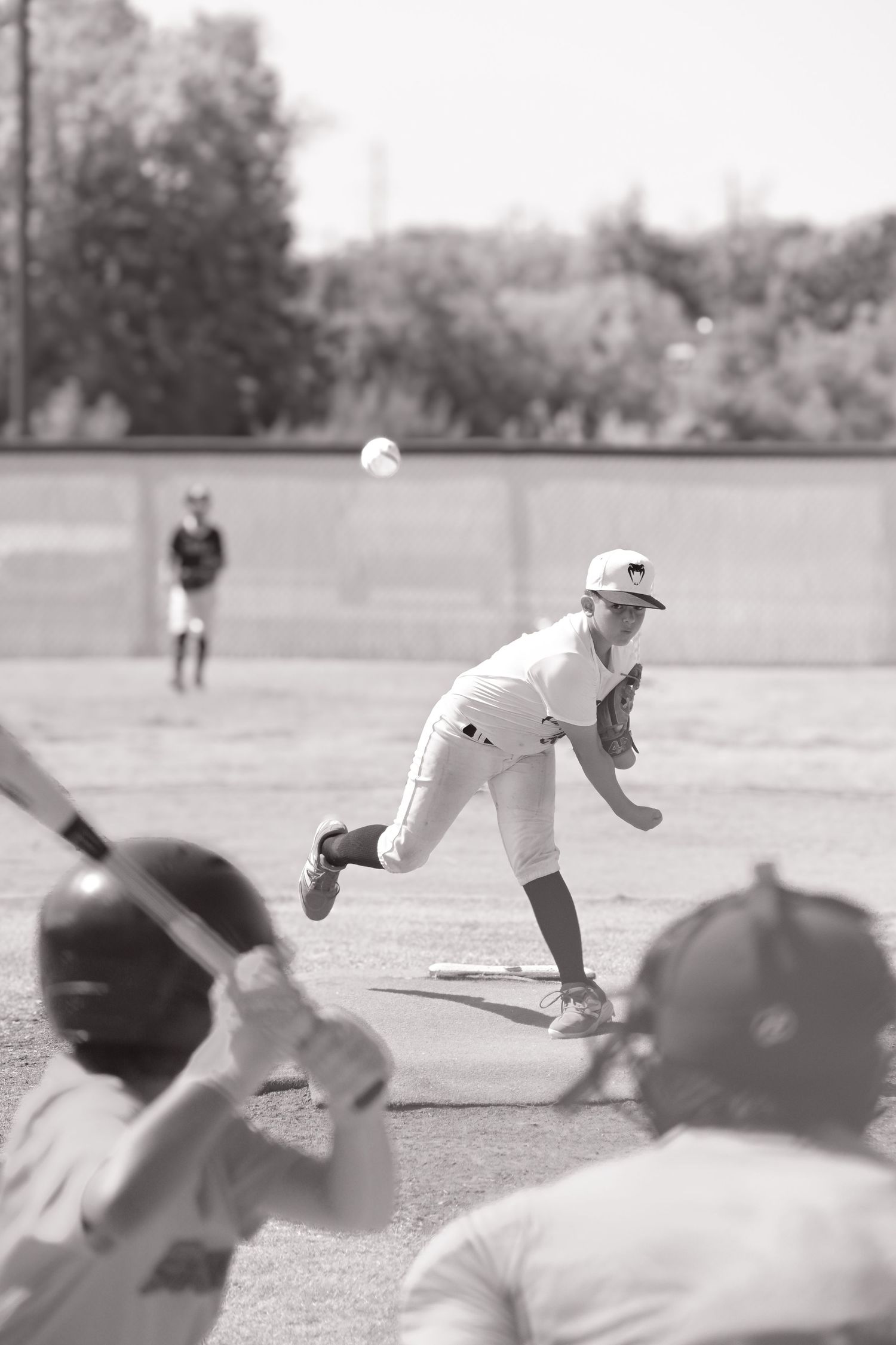 Black and white action shot of a pitcher throwing a ball toward a batter during a baseball game.