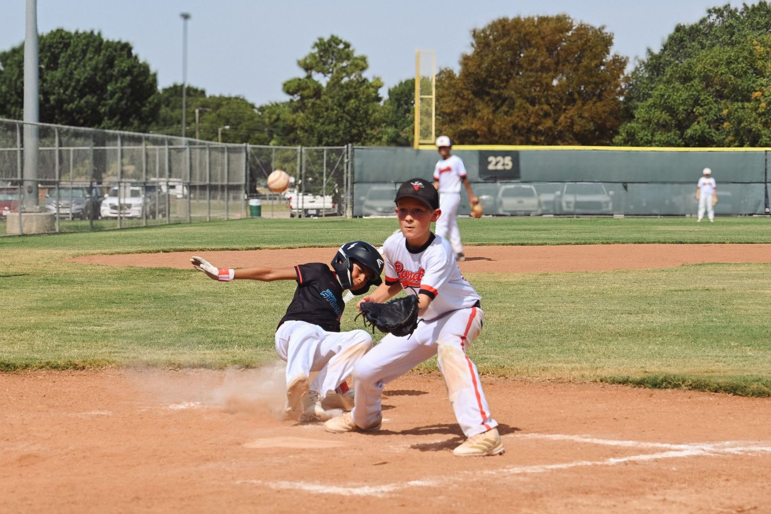 Youth baseball player slides into home plate as fielder attempts a tag during an intense game play.