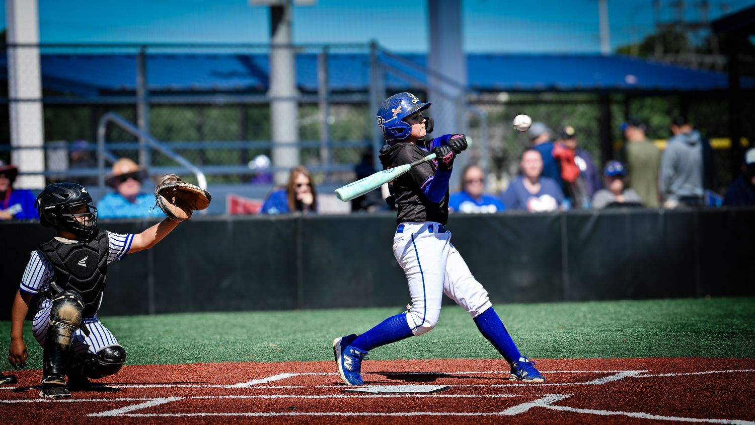 Blue uniform baseball player swings bat during competitive game with catcher behind home plate.