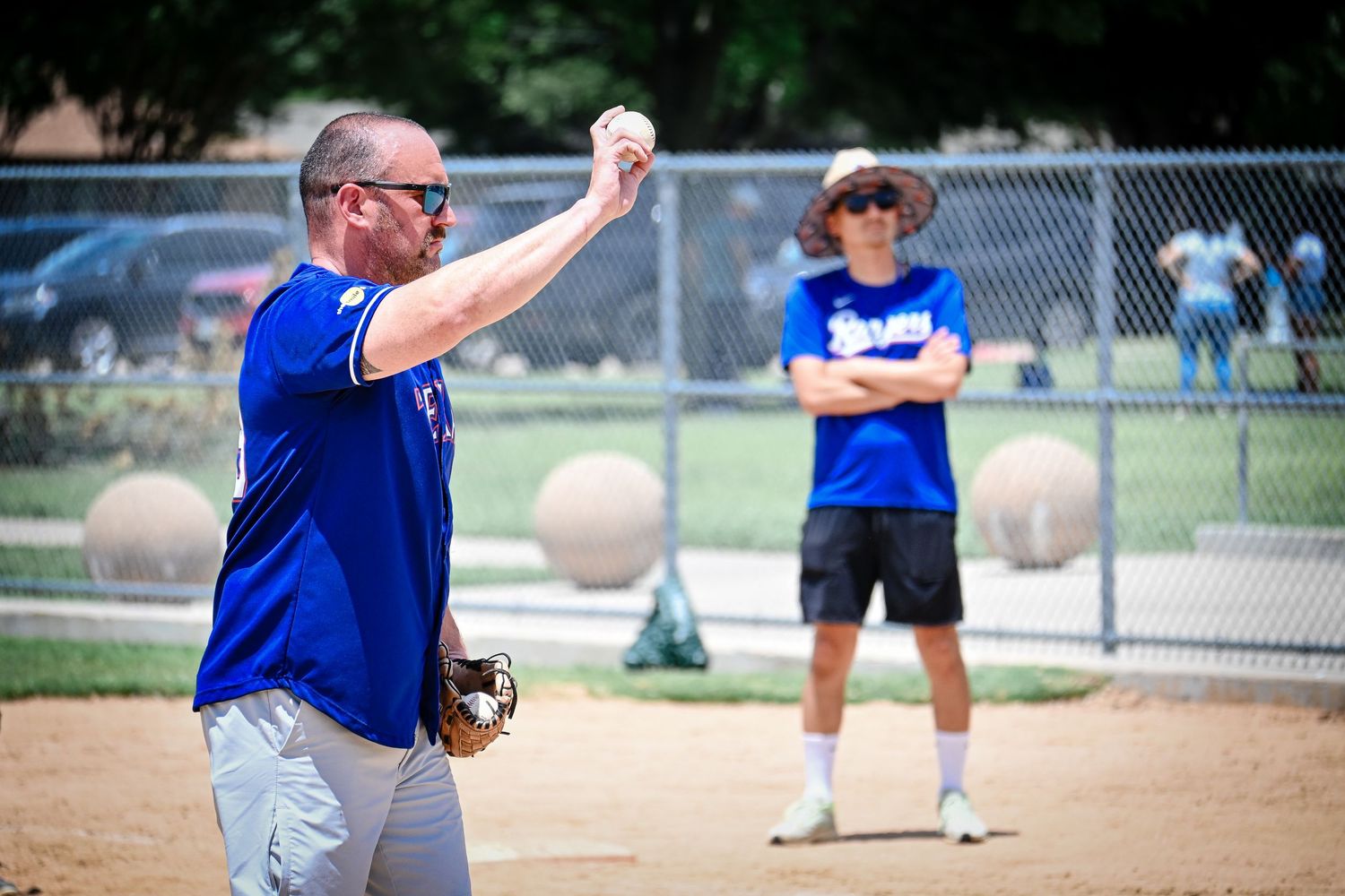 Adult male coach in blue jersey throwing a baseball during little league practice on sunny day.