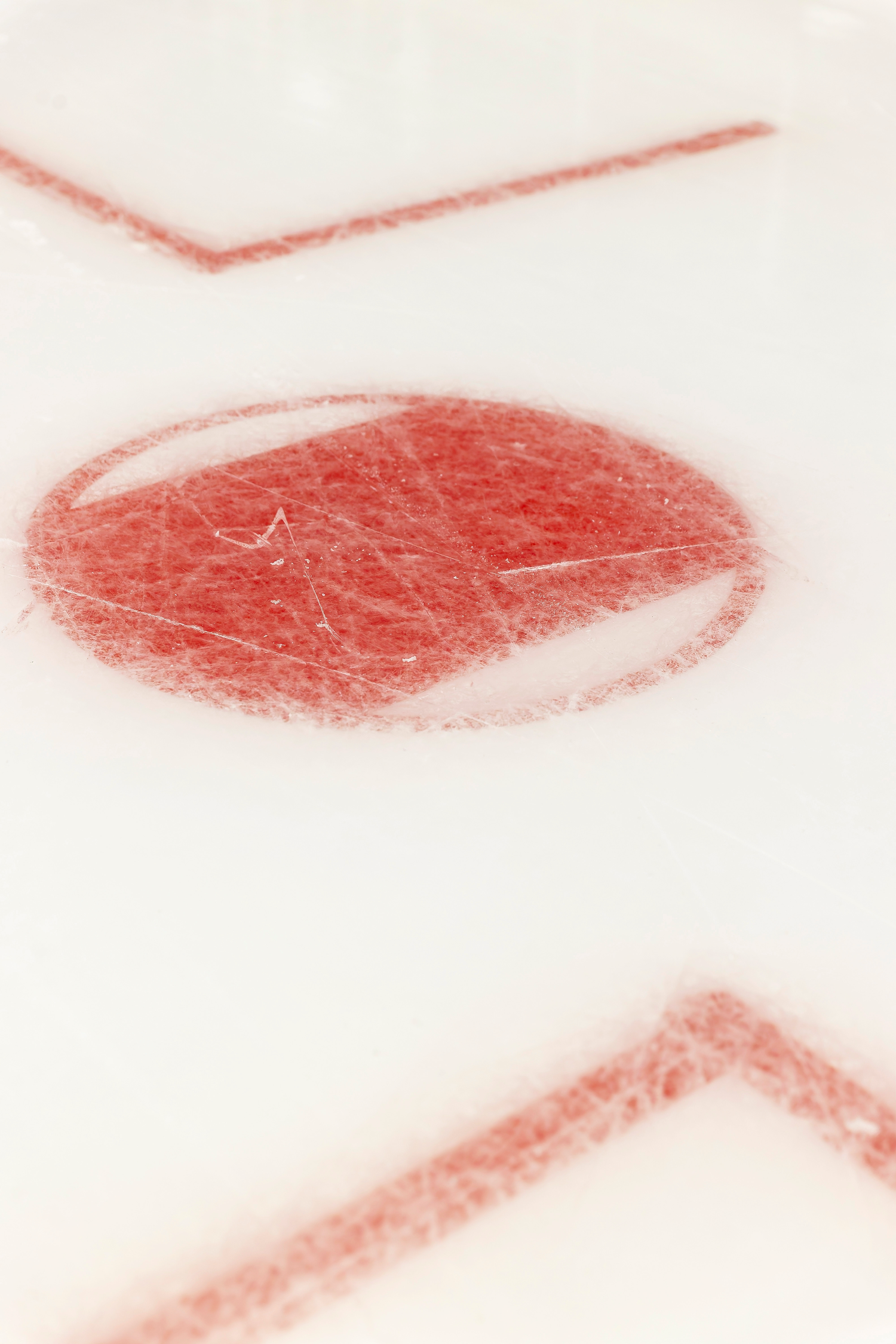 Close-up of a red hockey face-off circle and goal crease markings on white ice.