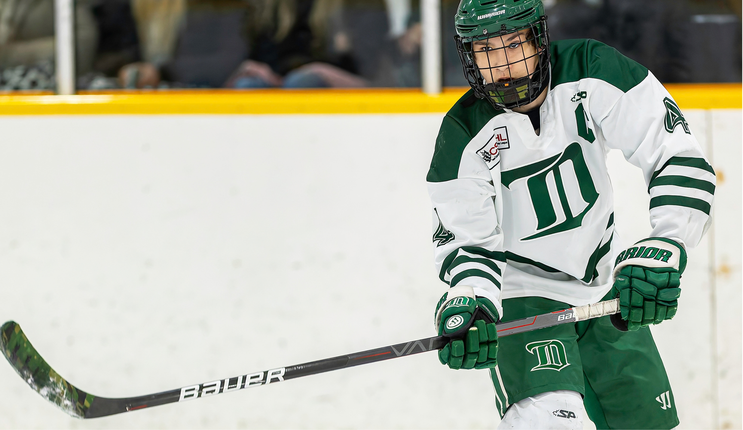 Hockey player in white and green Dartmouth uniform skating on ice rink during a college hockey game.