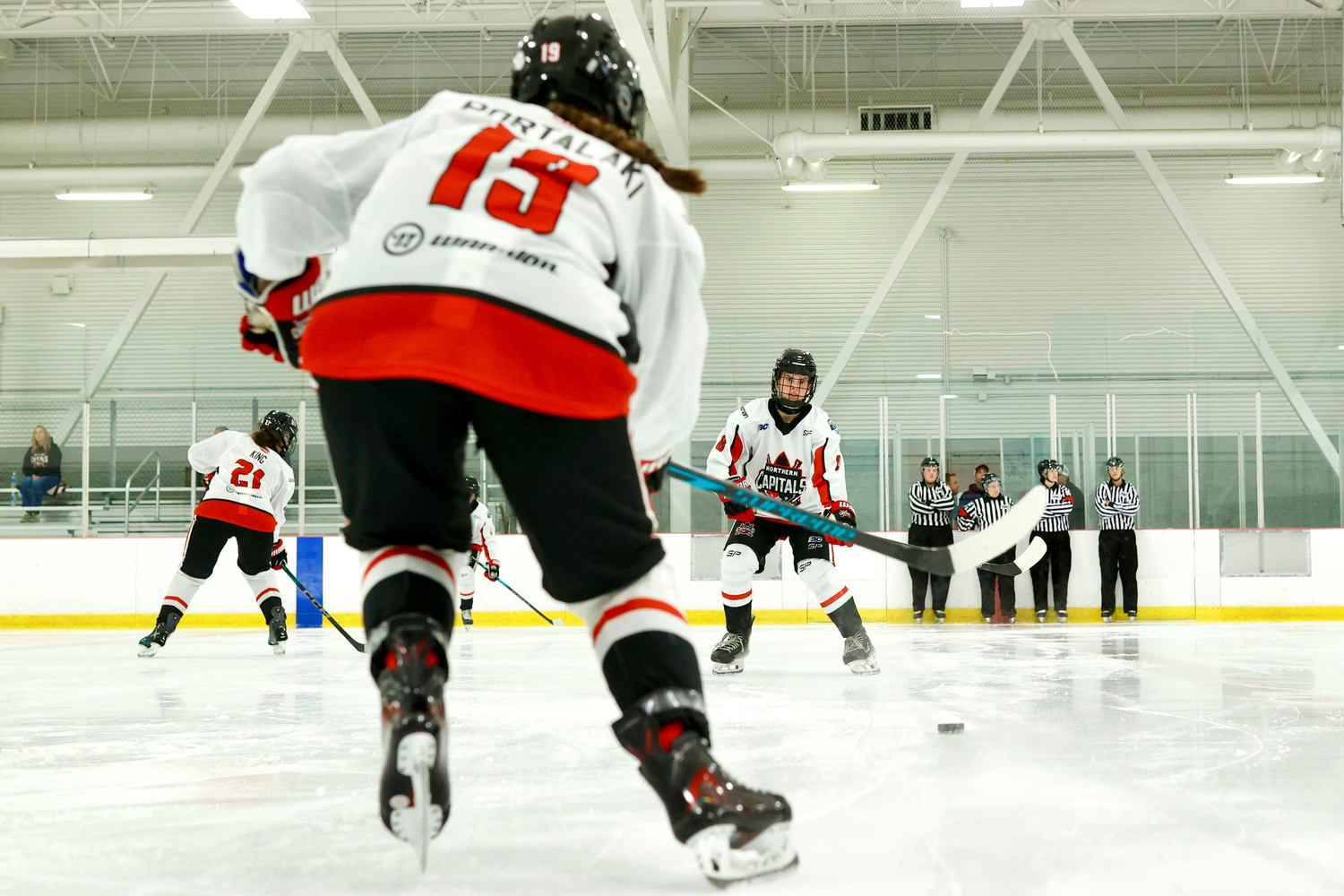 Youth hockey players in red and white jerseys practicing skating drills on indoor ice rink.