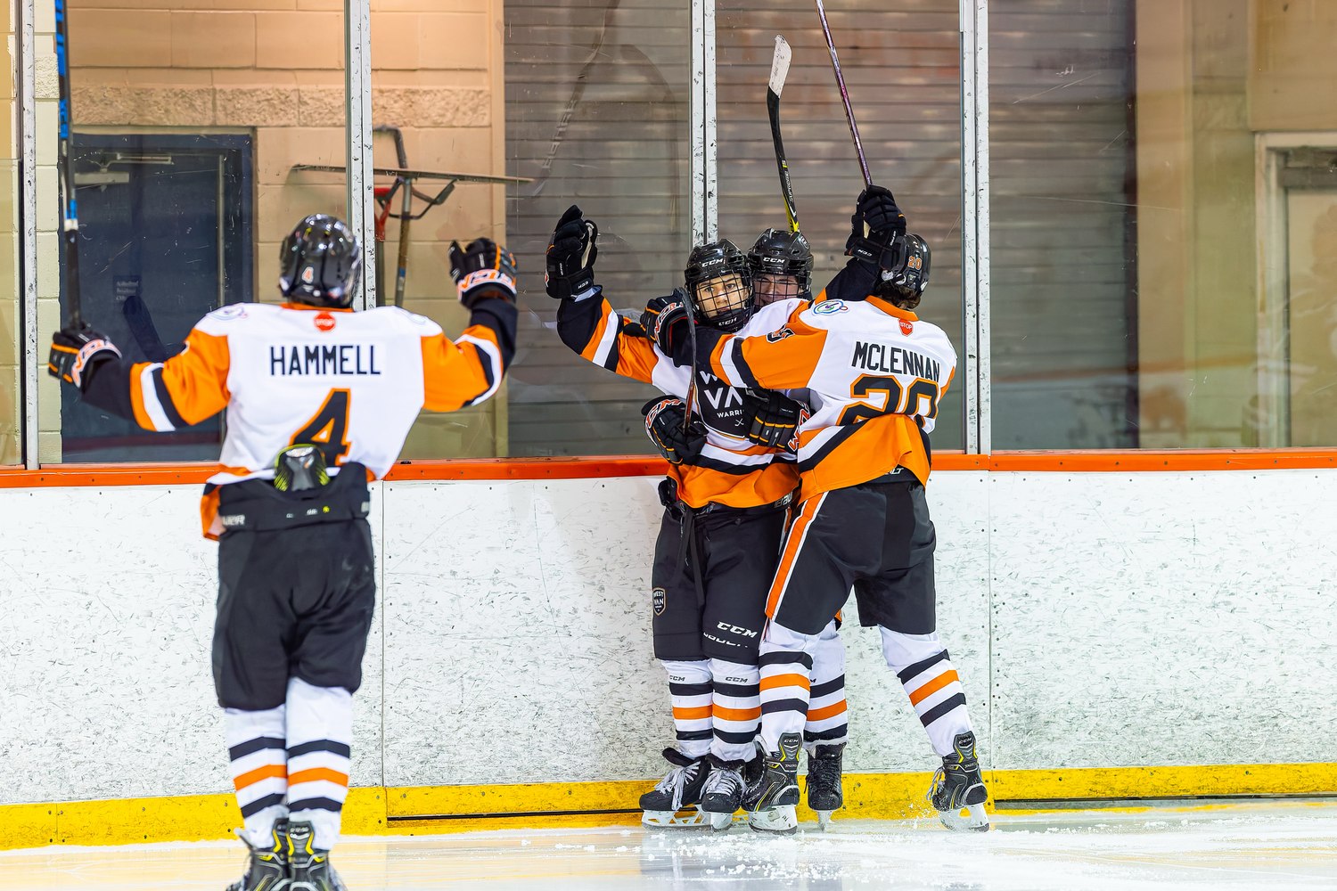 Hockey players in orange and black uniforms celebrate on the ice rink after scoring a goal.