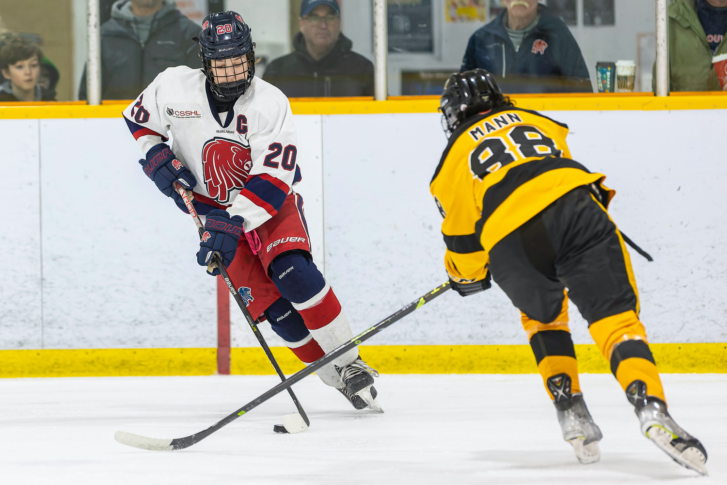 Hockey player number 20 in white uniform passes puck against opponent in black jersey.