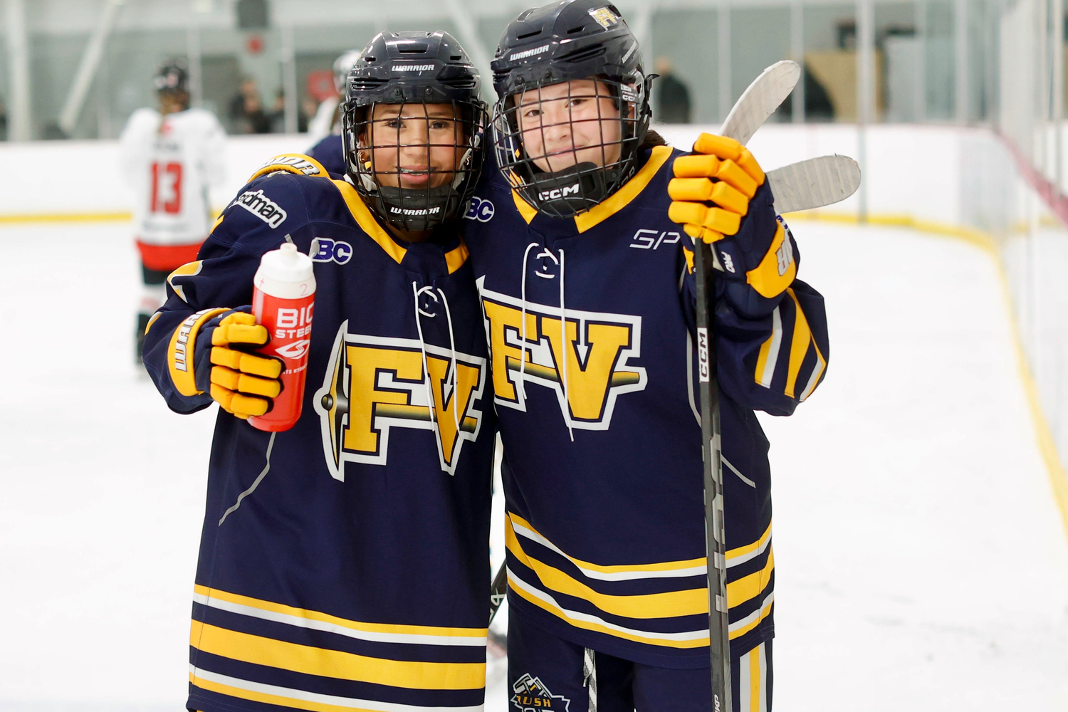 Two youth hockey players in FV navy and gold jerseys posing together on the ice rink.