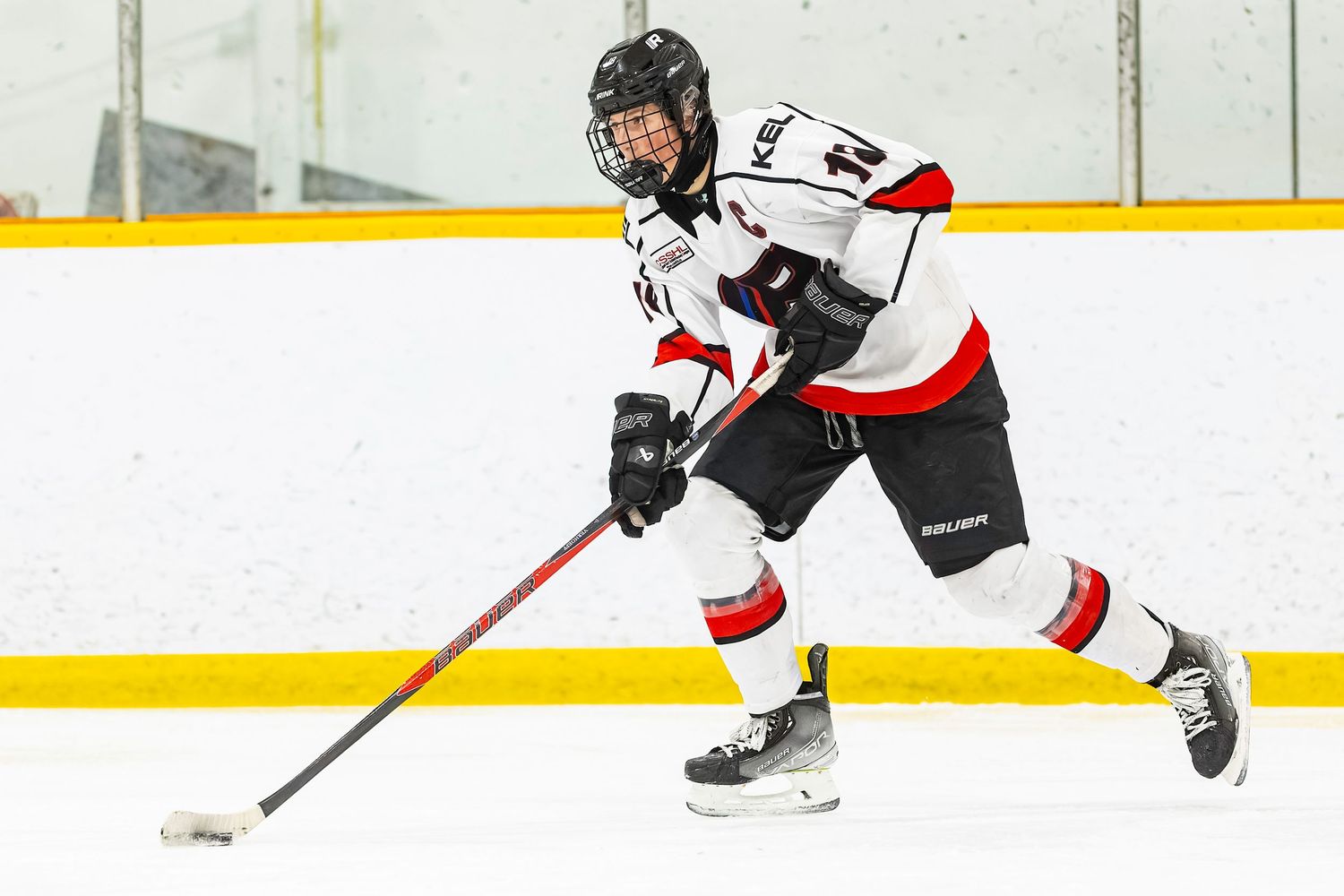 Hockey player in white and red uniform skating with puck on ice rink during game.