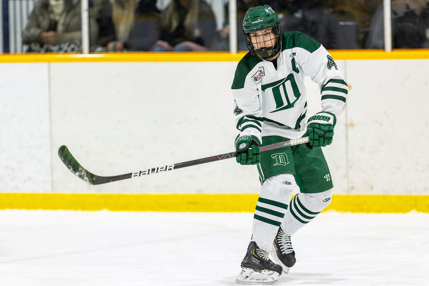 Female hockey player in green white uniform skating on ice during competitive game.