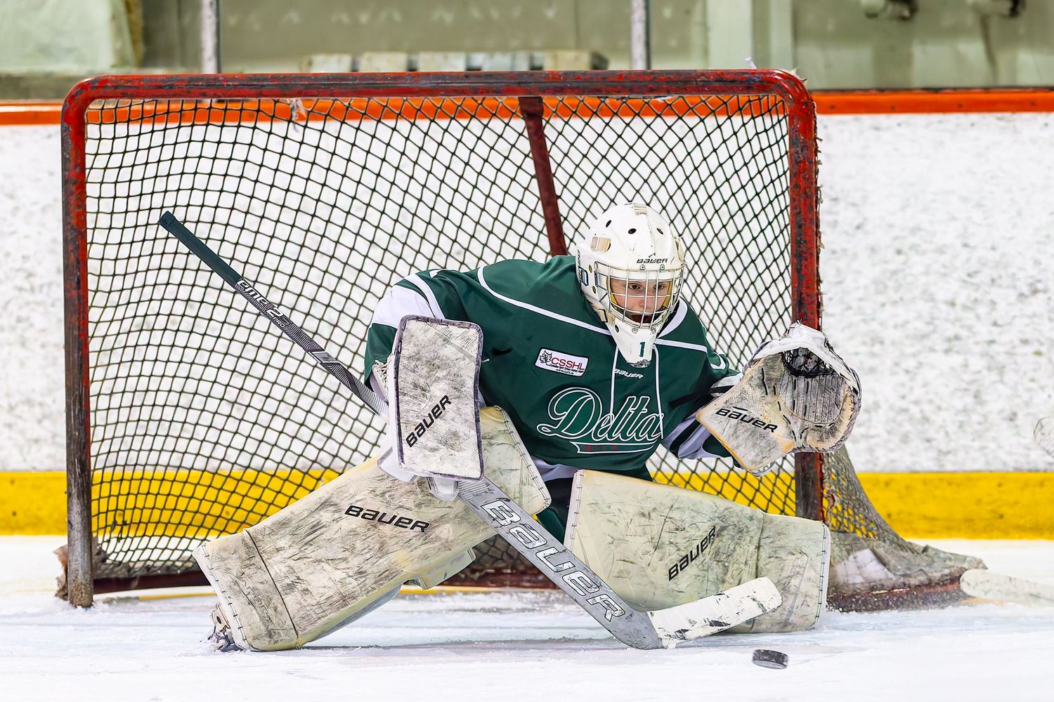 Ice hockey goalie in green uniform making a save in front of the net during a game.