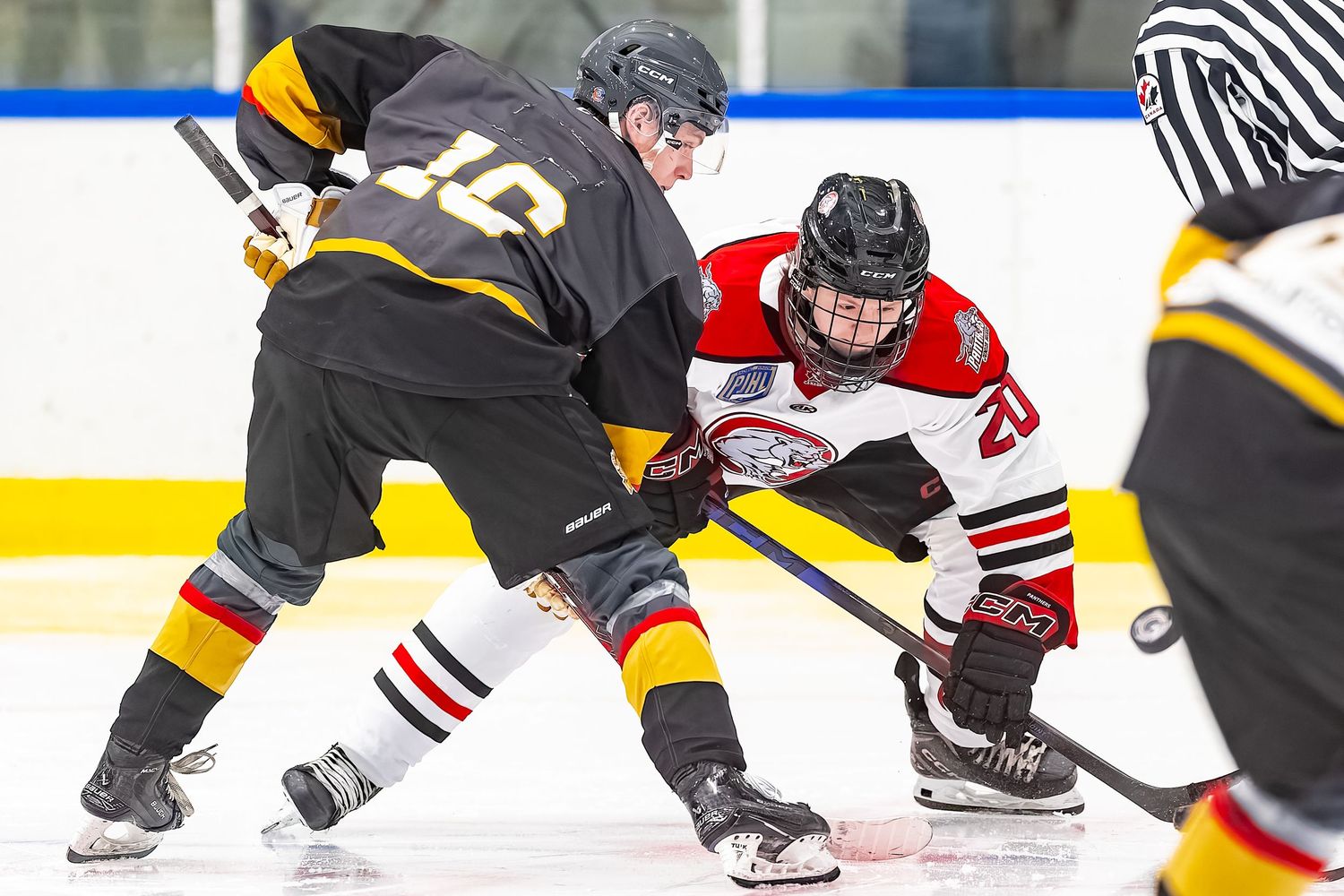 Two ice hockey players face off at center ice during a competitive game, wearing black and red uniforms.