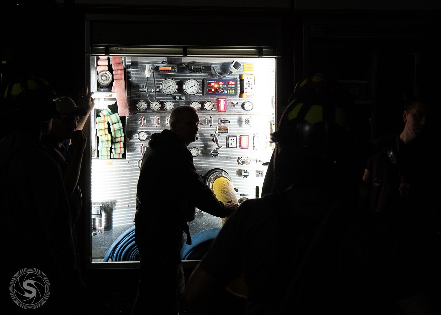 Silhouetted firefighters operating a fire truck control panel at night during an emergency response.