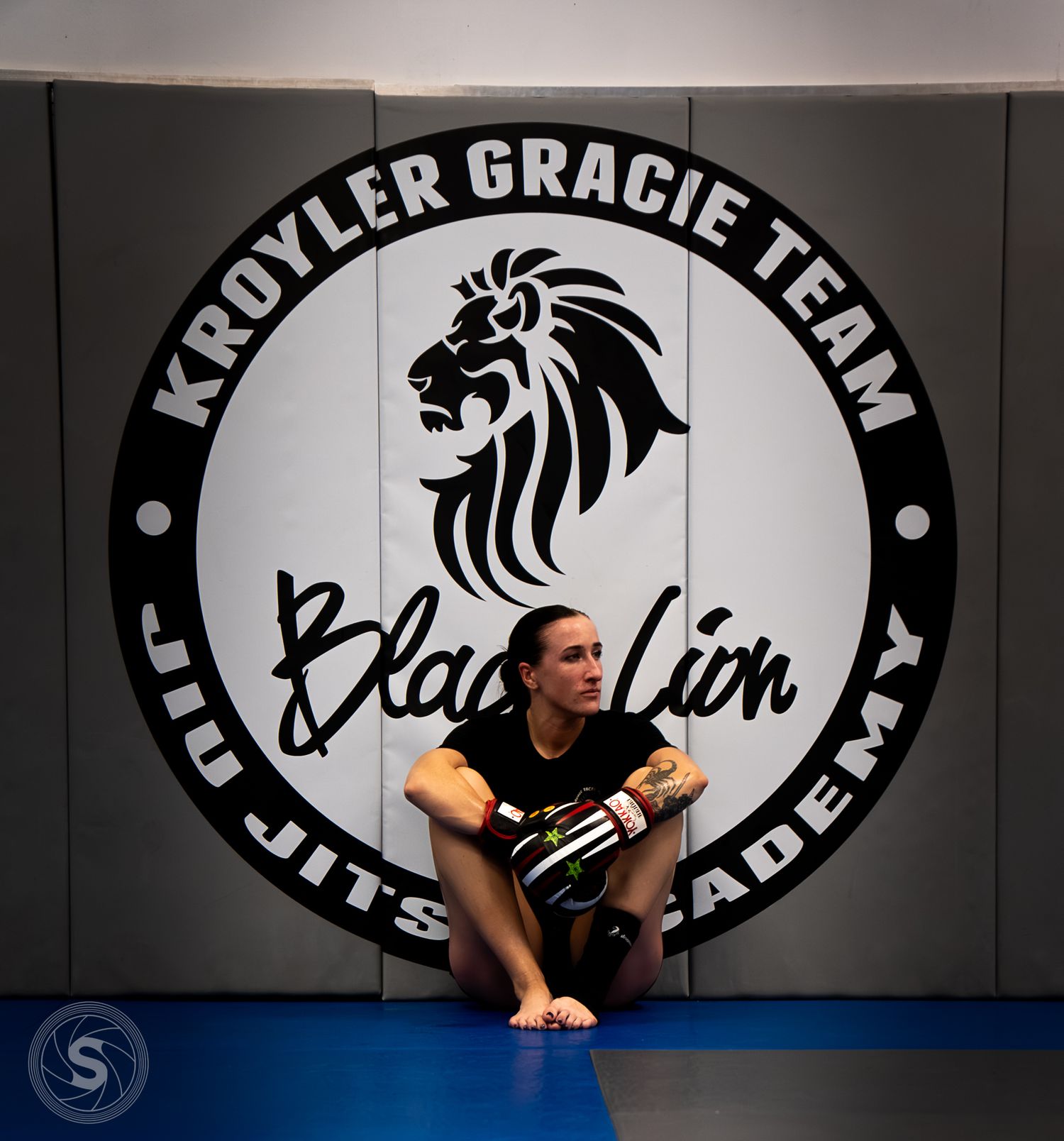 Female martial artist sits on mat at Kroyler Gracie Team Black Lion Jiu Jitsu Academy gym.