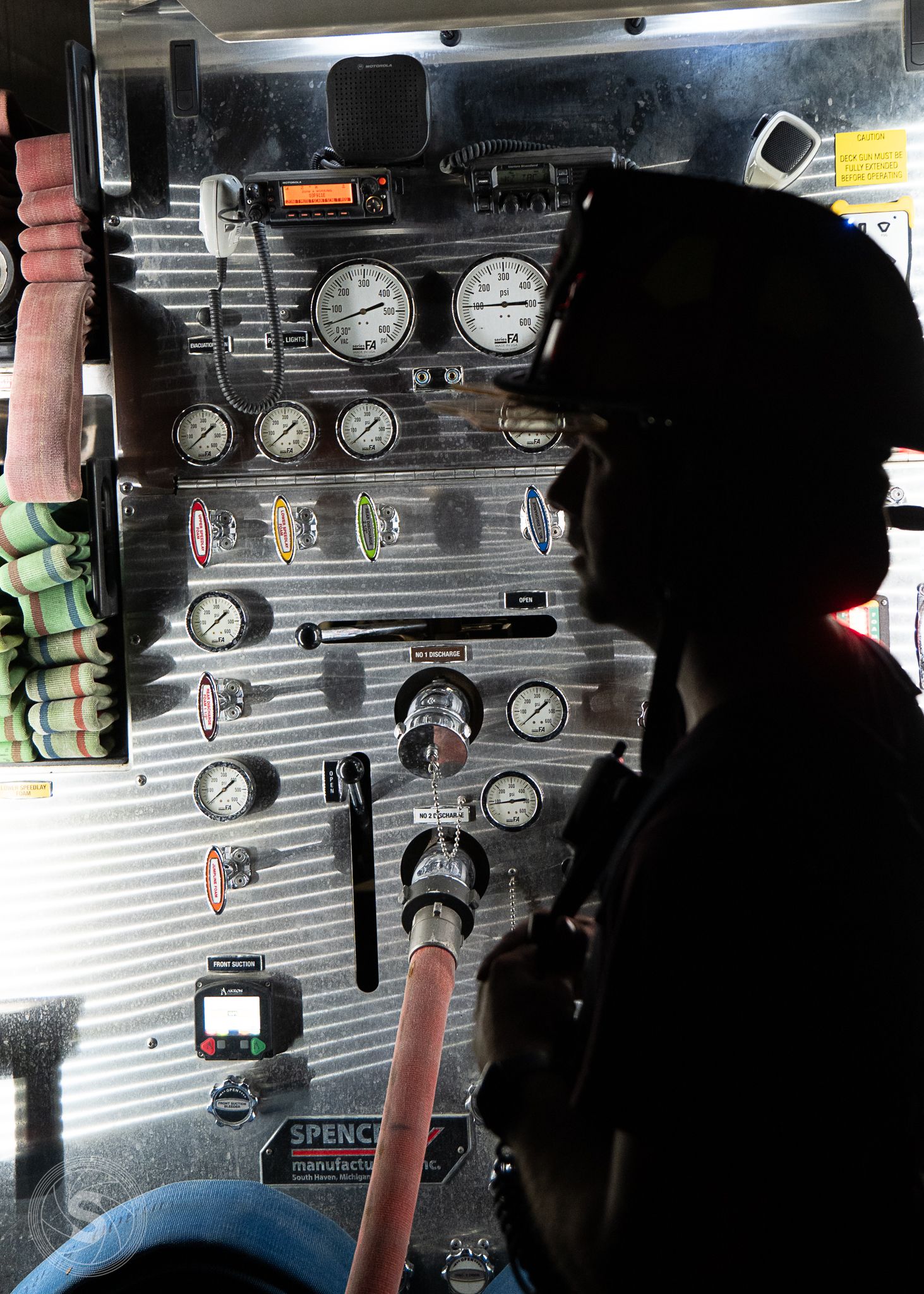 Silhouette of firefighter operating pressure gauges and controls on a fire truck pump panel.