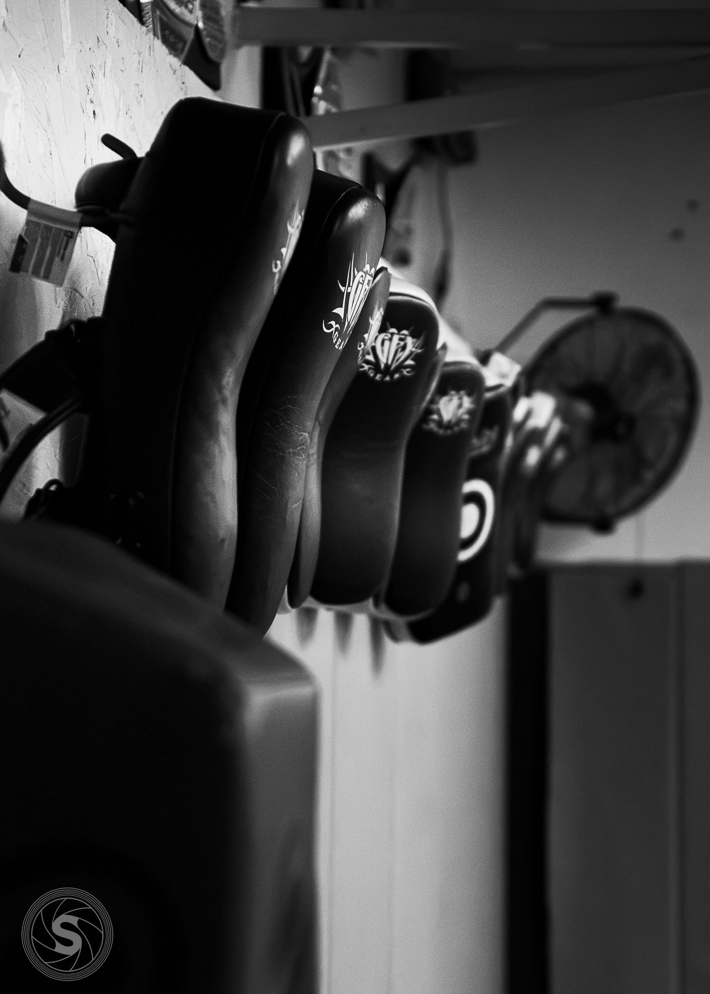 Black and white photo of roller skates on a rack with a fan in the background.
