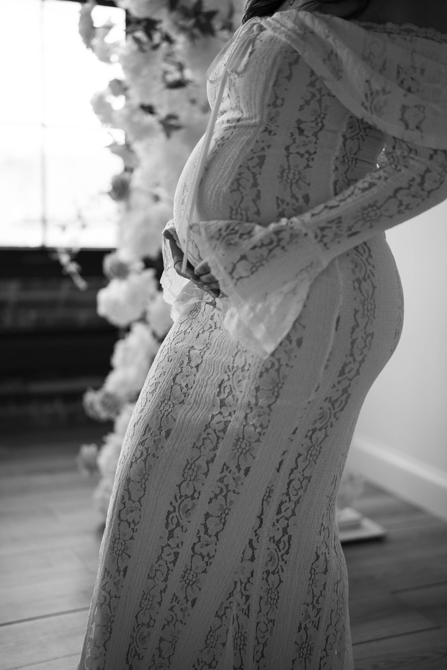 Close-up black and white detail of lace maternity gown with floral elements.