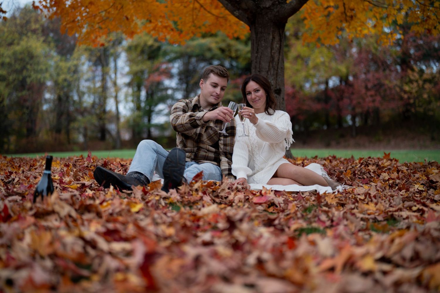 Colorful autumn leaves scattered on the ground create a cozy backdrop for an outdoor portrait session in a park setting.