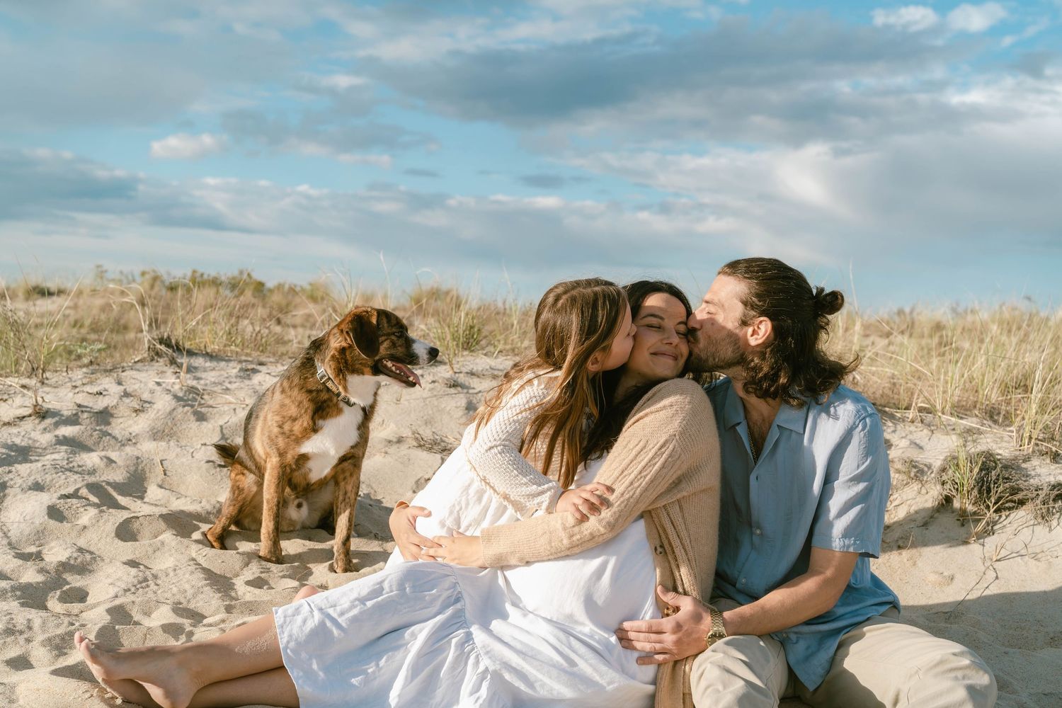Beach photoshoot featuring couple lounging on sand with dog nearby.