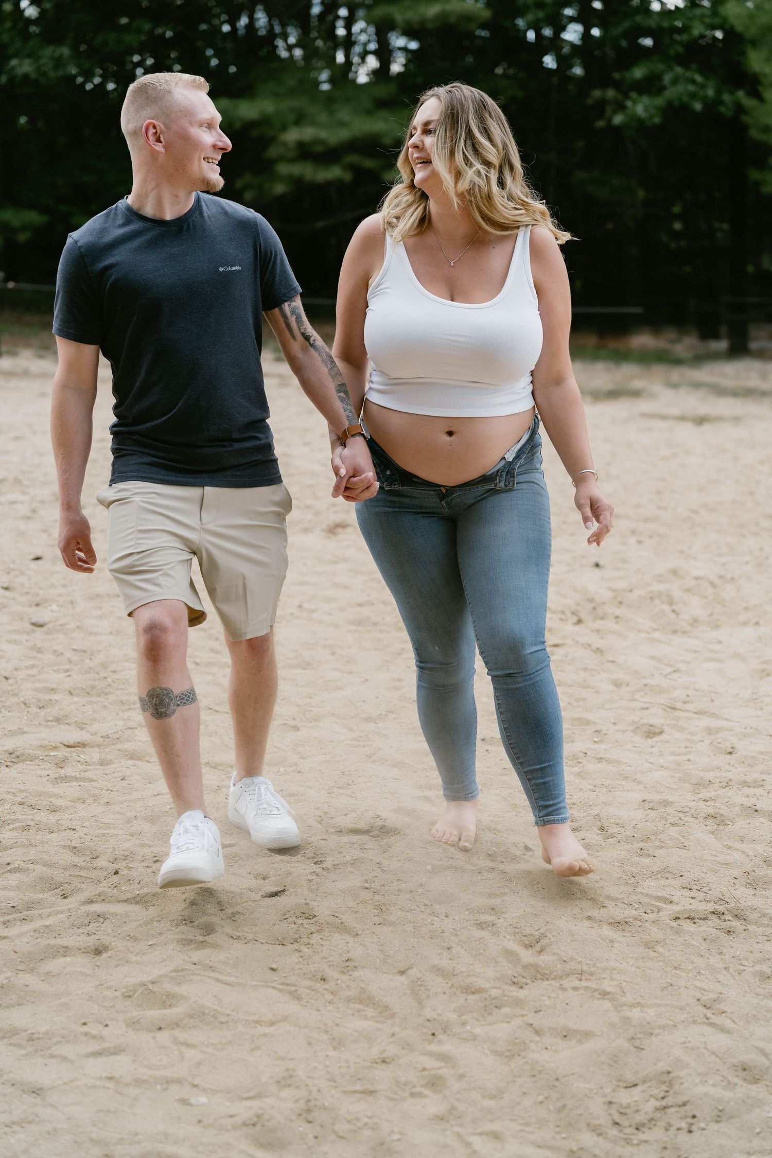 Couple walking barefoot together on sandy beach, showing casual summer attire.