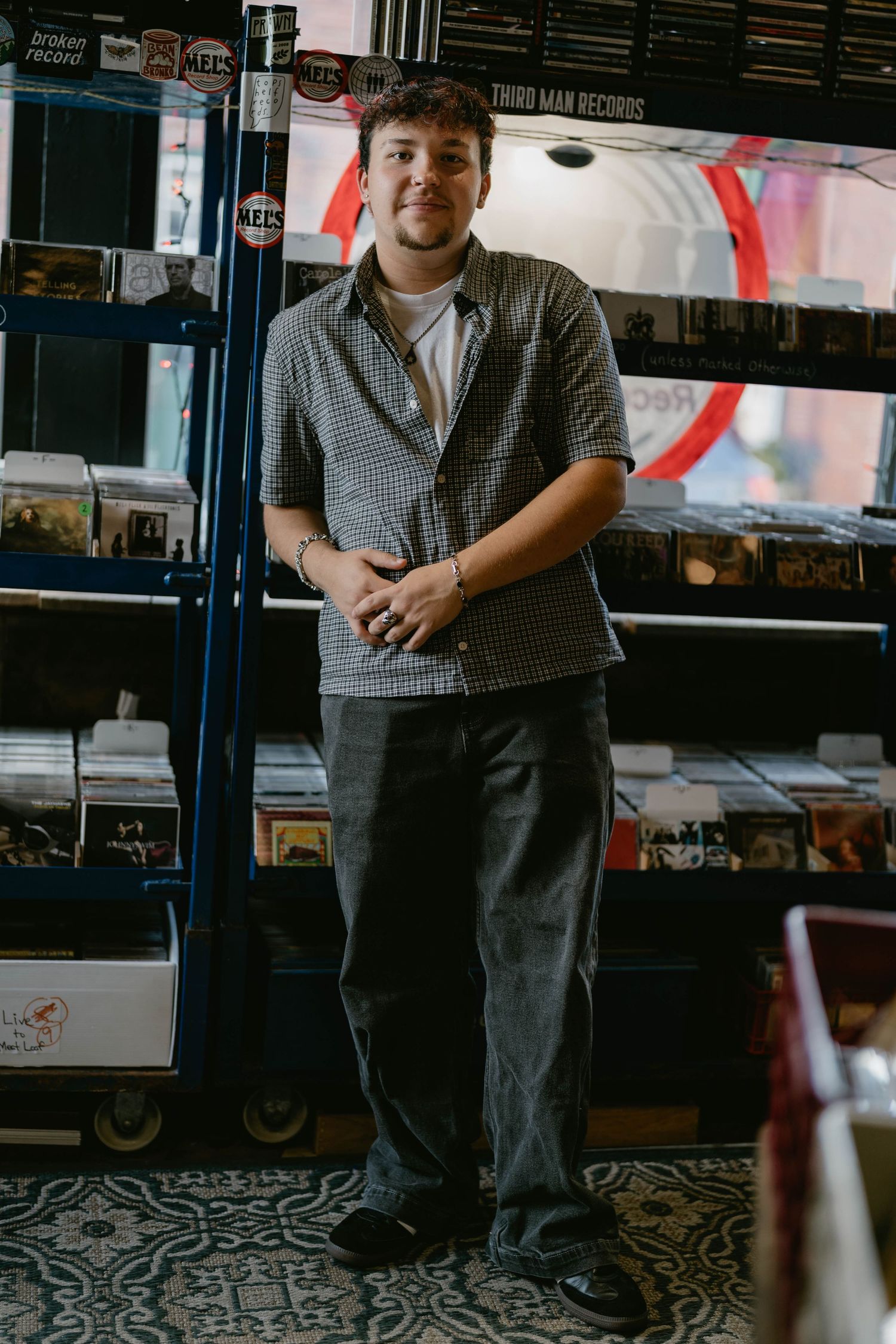 Teen standing near stacks of vinyl, relaxed pose and candid smile.