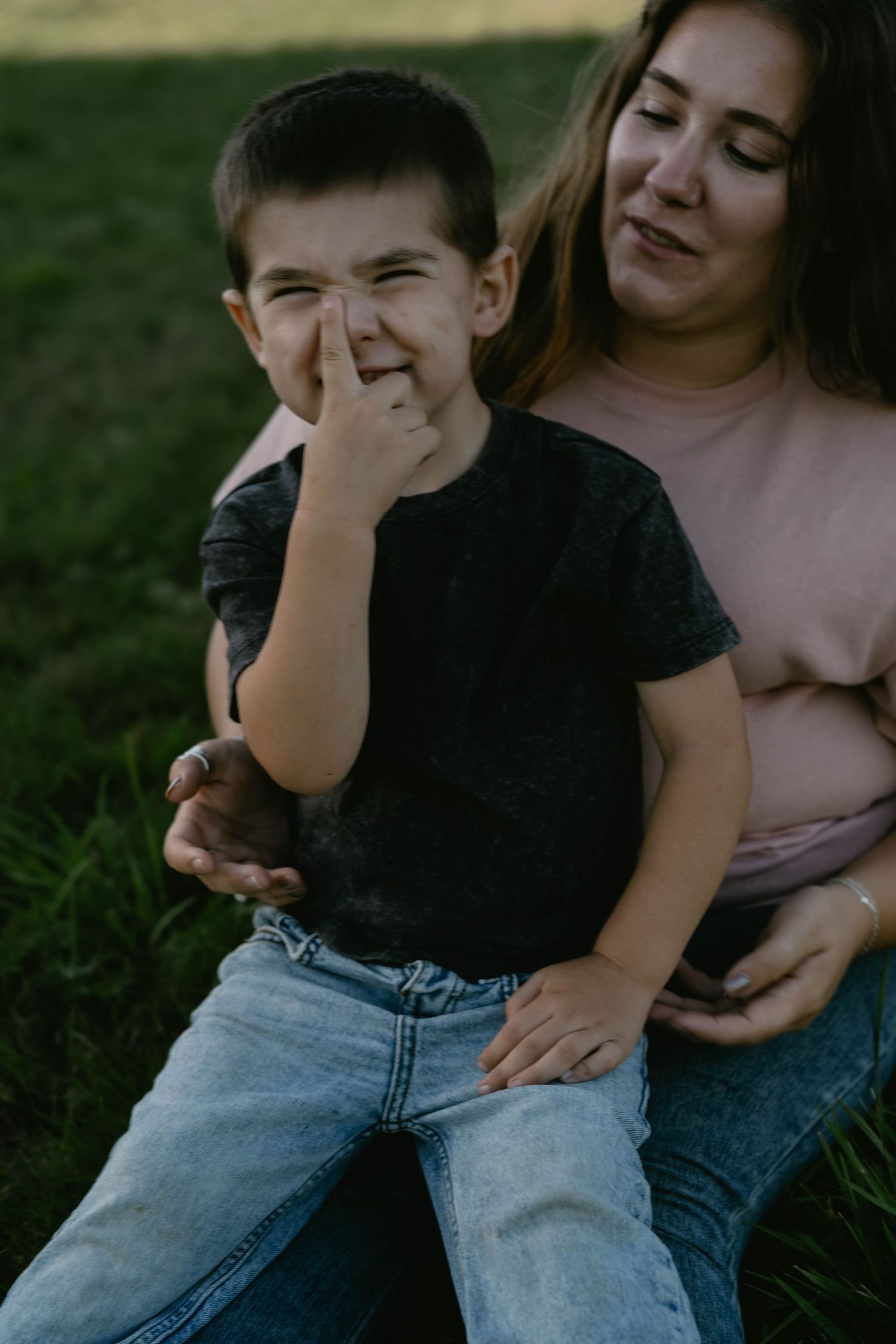 A joyful moment captured outdoors as a young child in a black t-shirt laughs while sitting on grass with a companion.