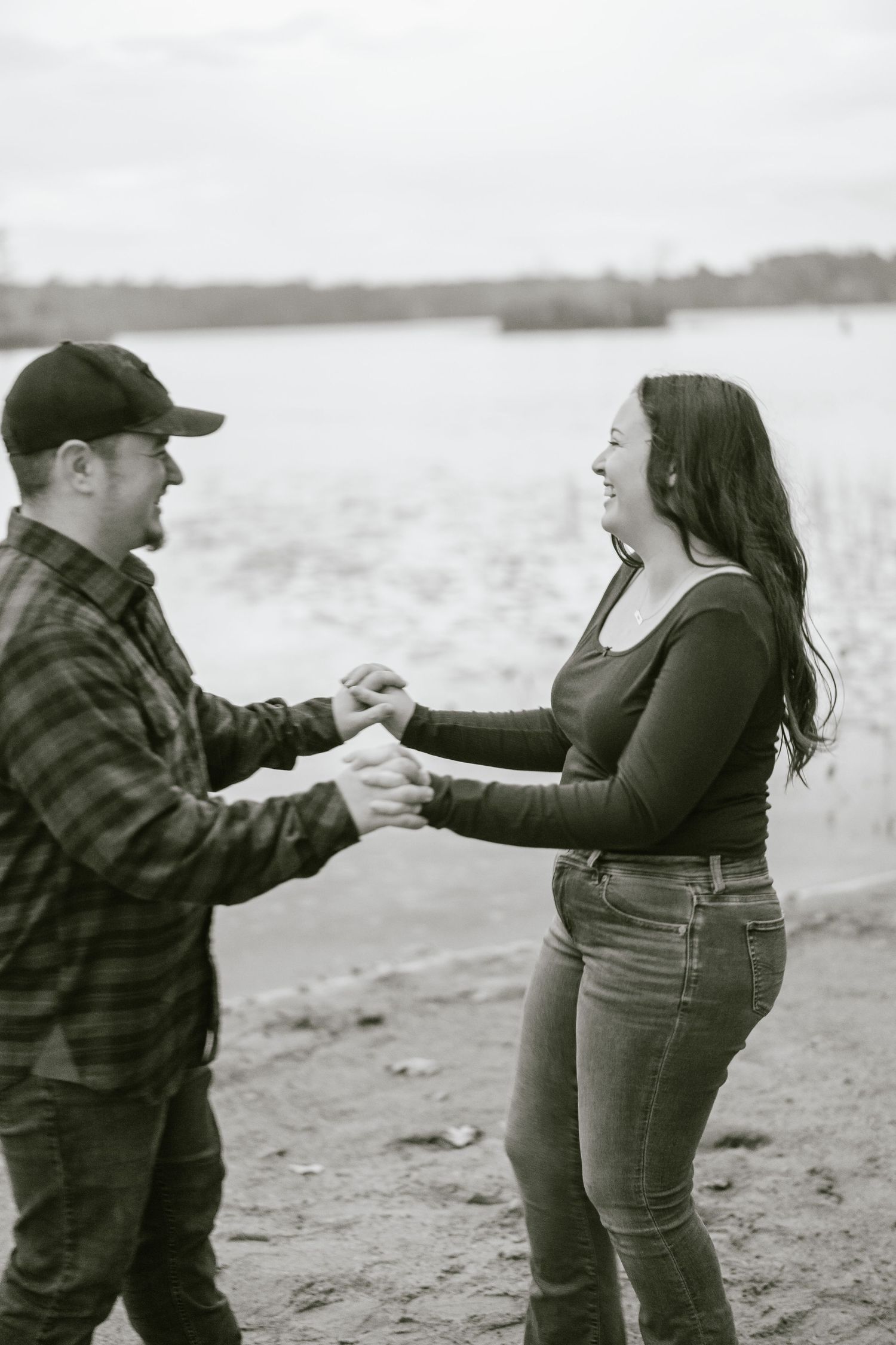 A couple shares a joyful moment dancing together on a beach with water in the background.