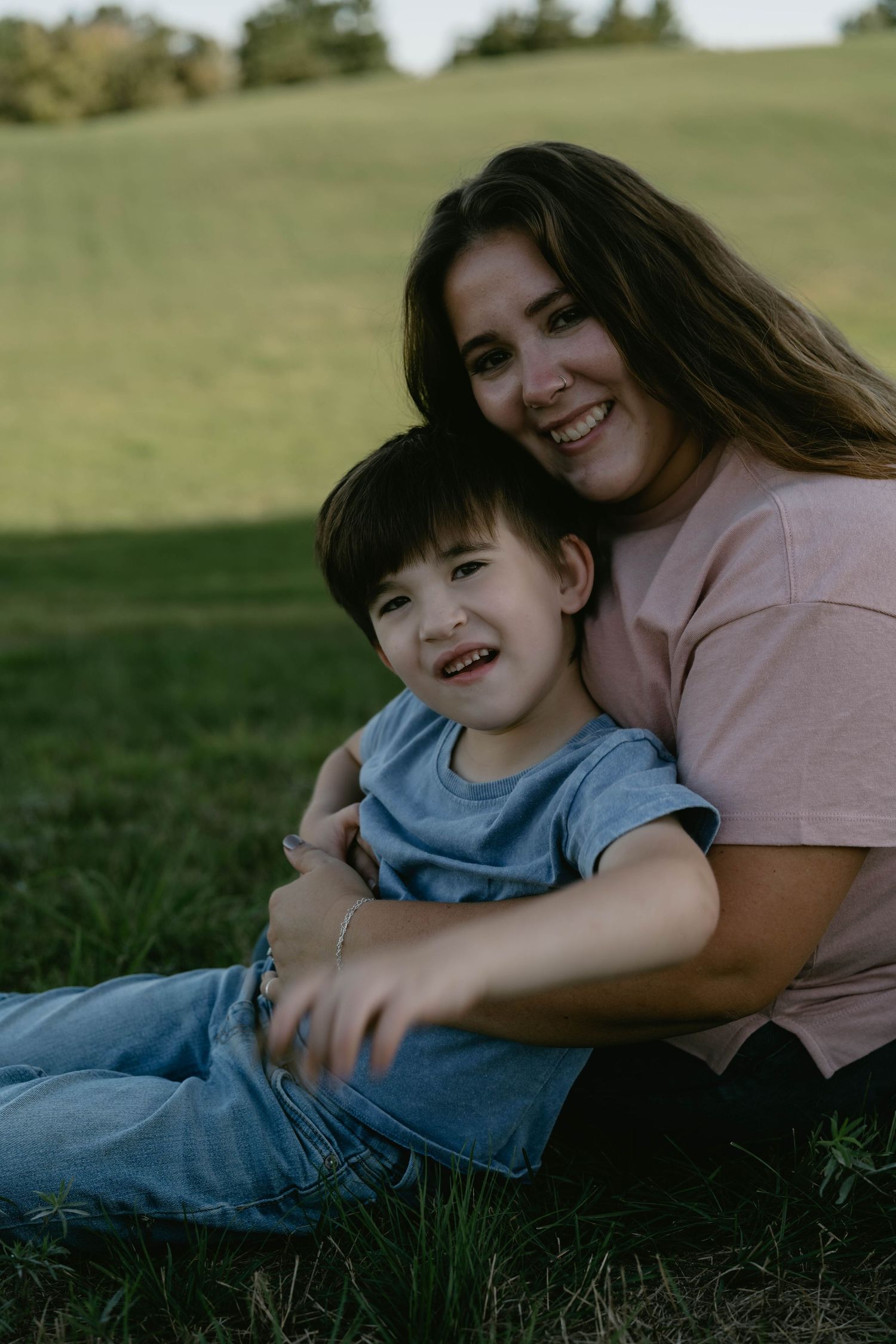 A pair relaxes together on green grass during a warm outdoor photoshoot in natural lighting.