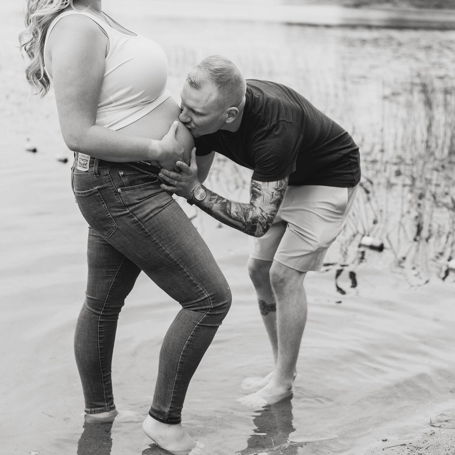 Couple playfully interacting near water's edge in black and white photography.