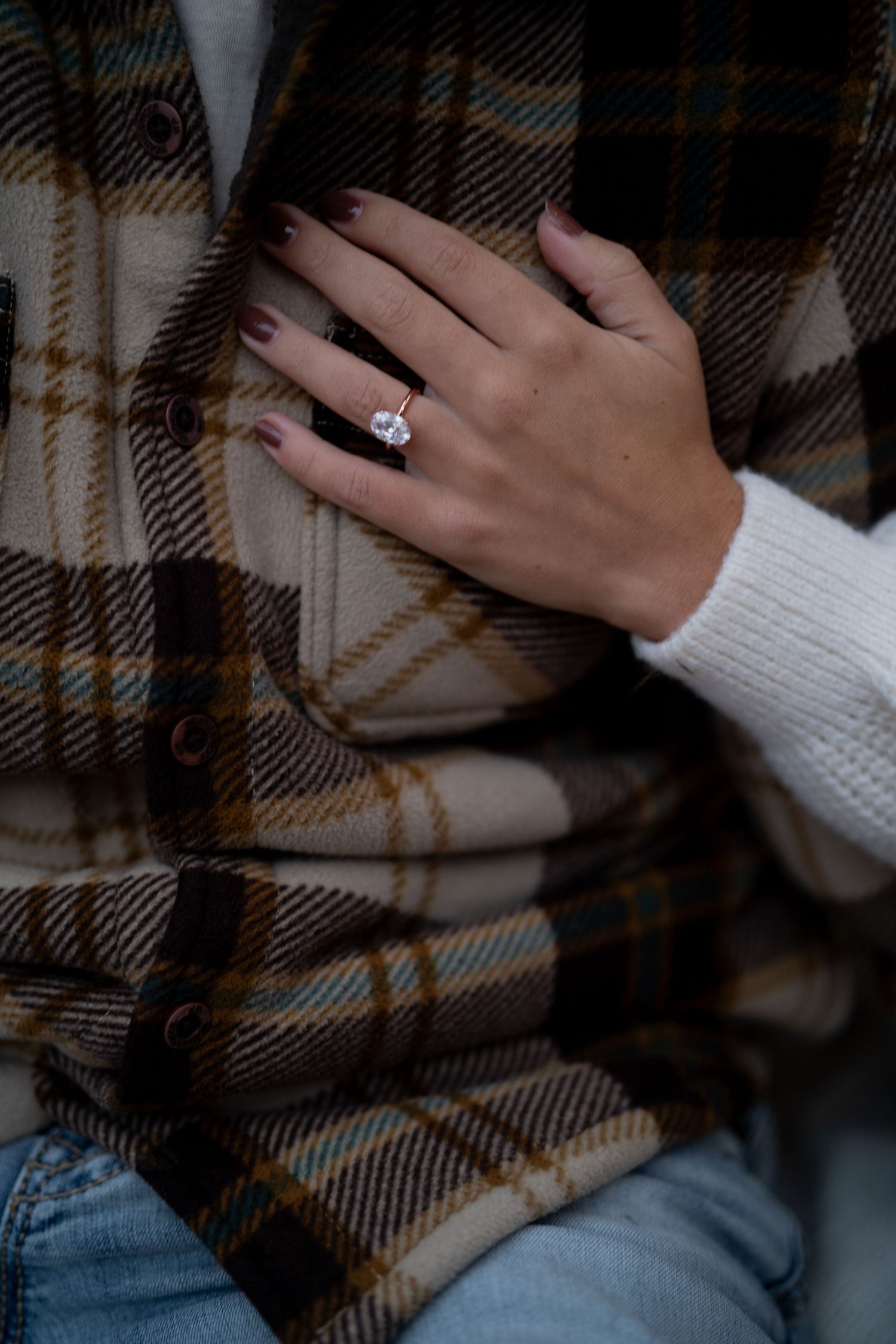 Hands wearing a white sweater rest on a plaid blanket with blue jeans in a cozy indoor setting.