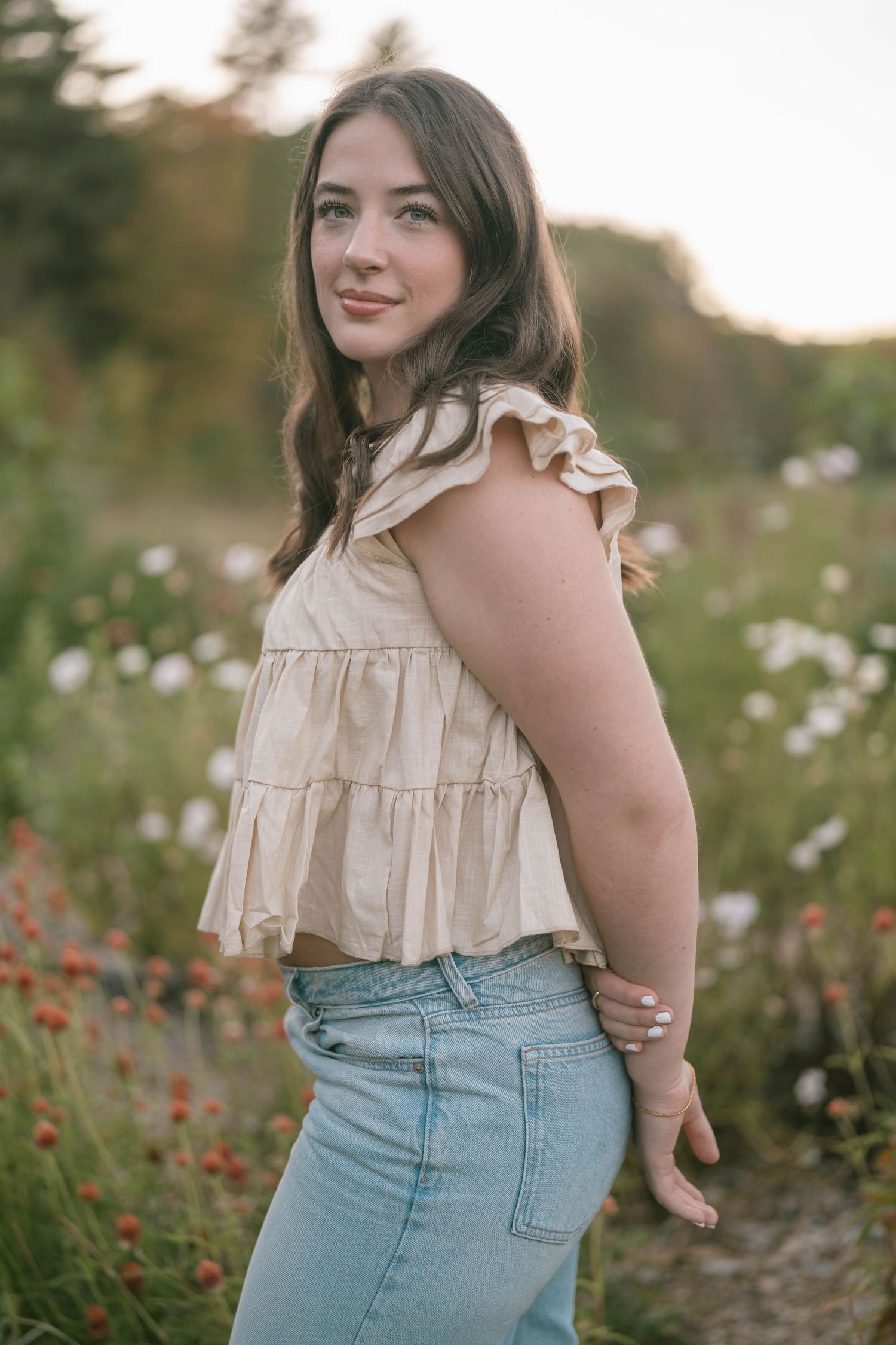Teen standing with arms outstretched in a blooming field, light and airy portrait.