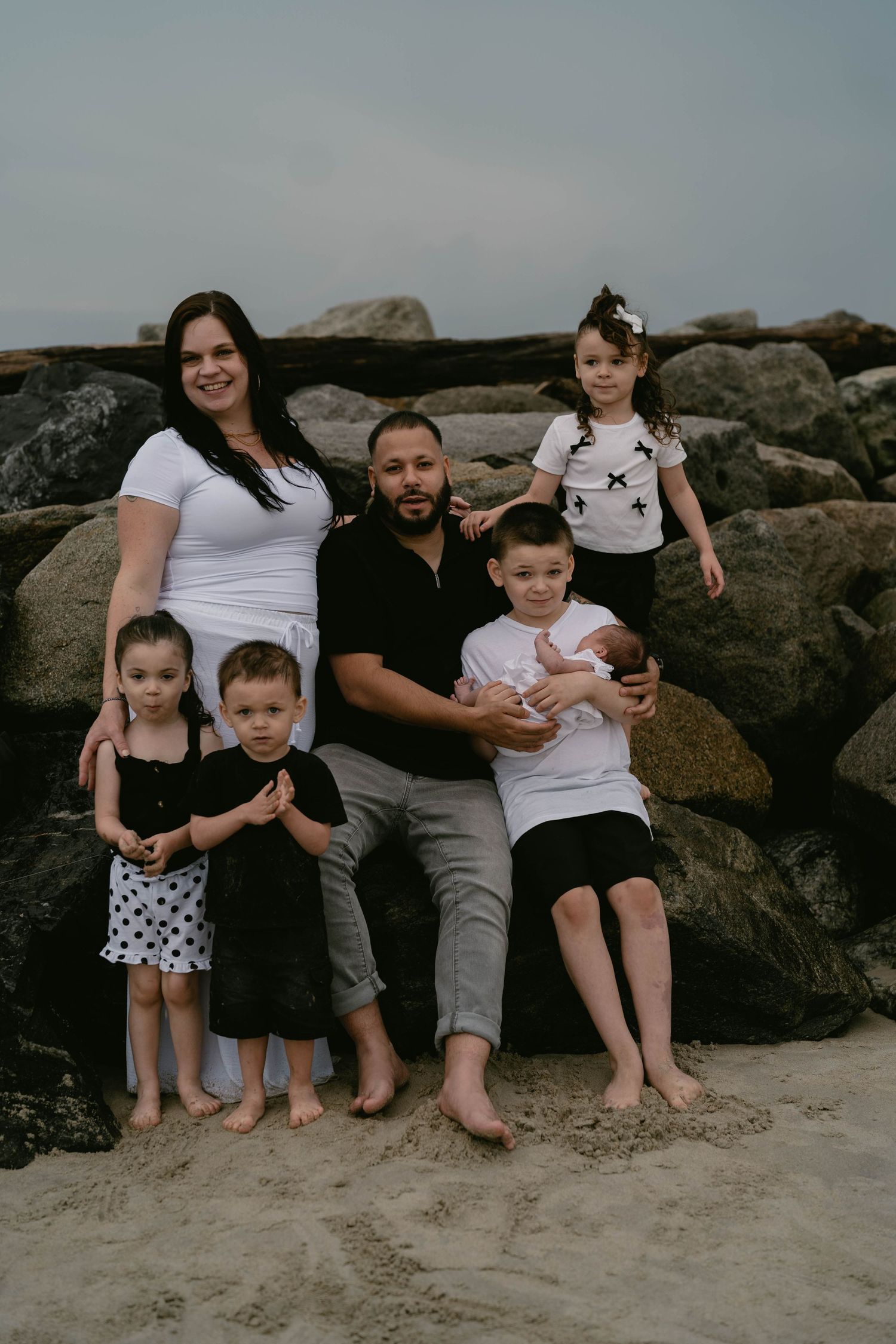 Extended family sitting together on rocky beach during overcast day.