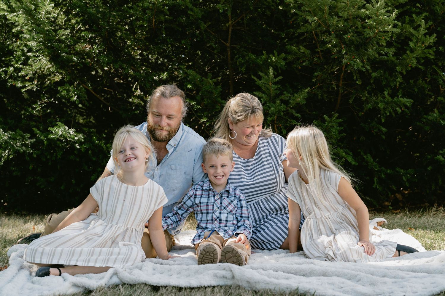 Family portrait session outdoors with everyone laying on a white blanket in nature.