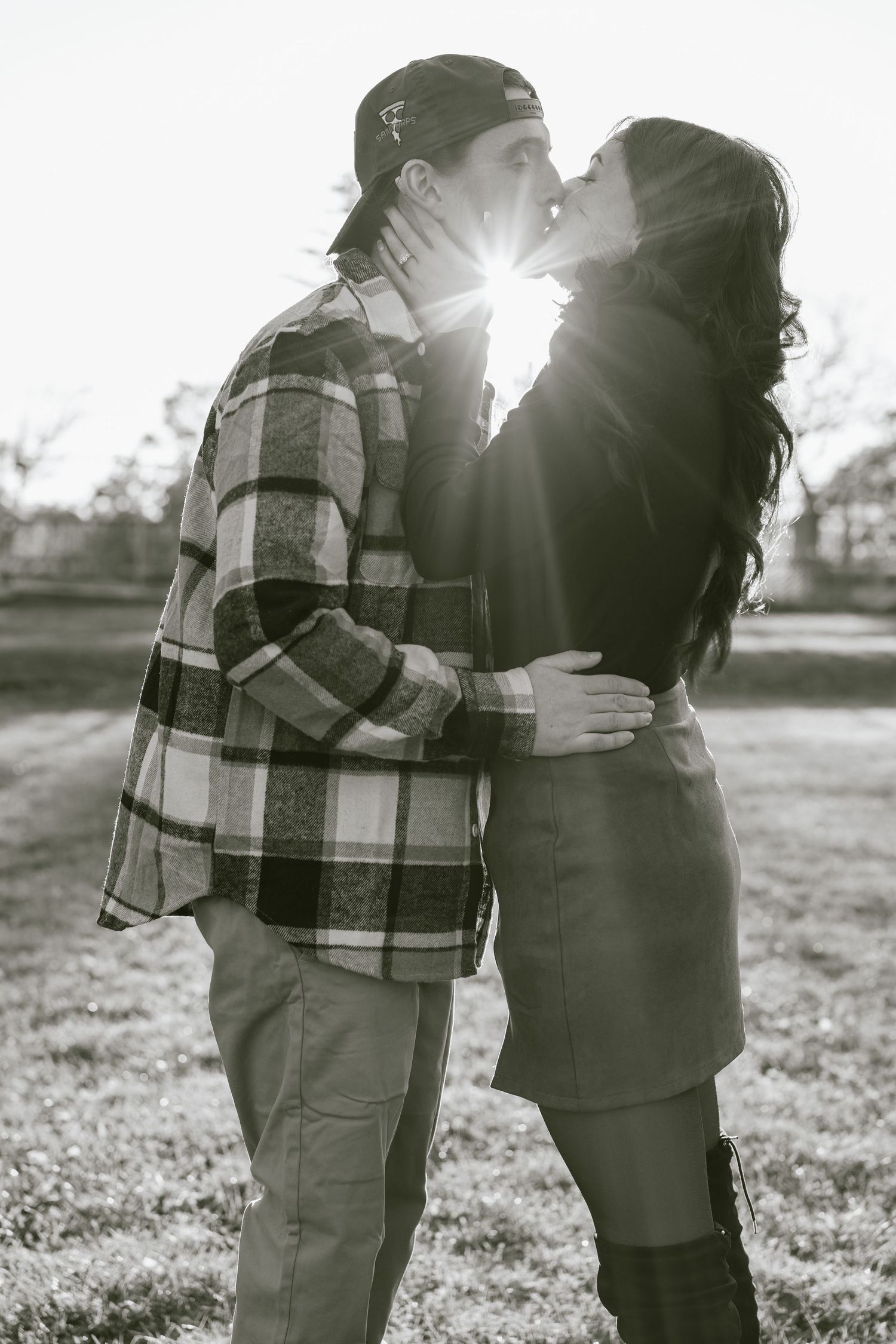 Black and white photo of a tender embrace in a field with sunlight streaming through the background.