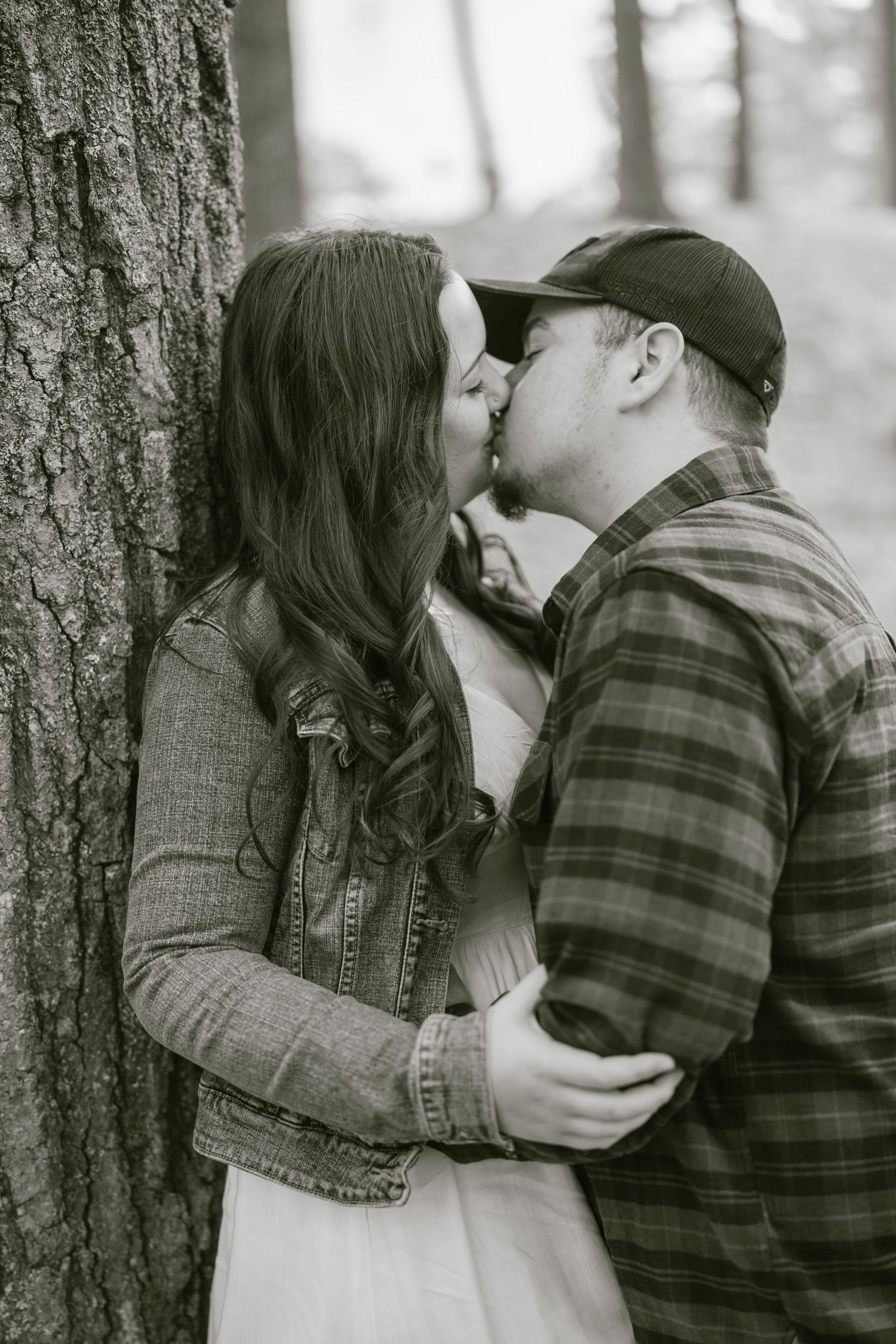 Romantic couple sharing a tender moment against a tree trunk in black and white.