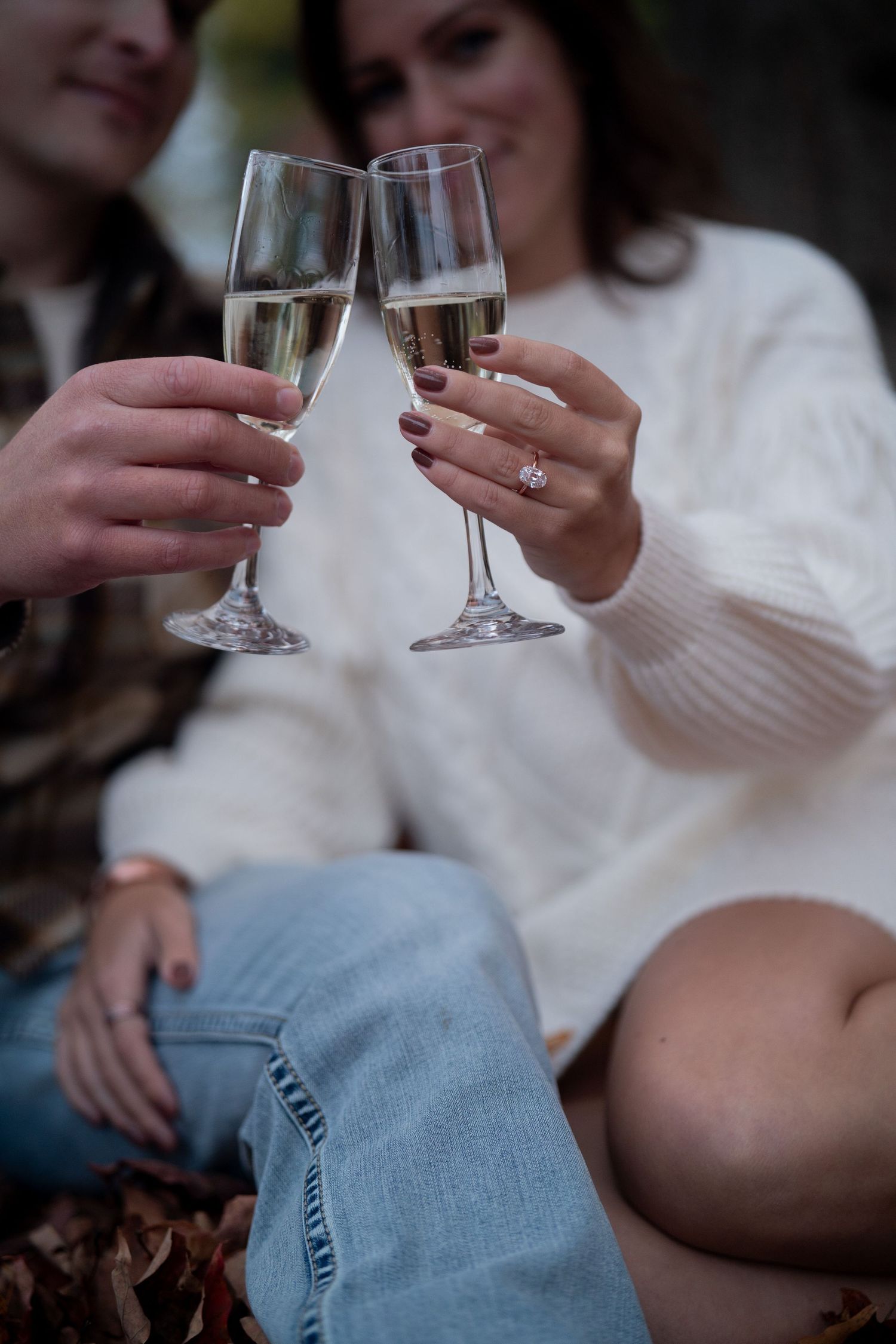Two people in white sweaters holding wine glasses together in a cozy indoor setting.