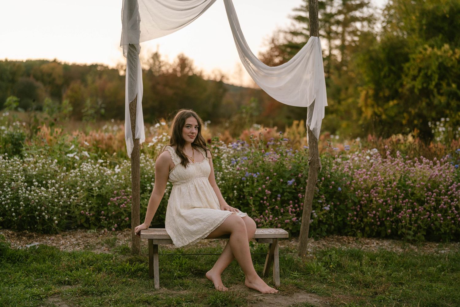 Senior sitting on a bench in a colorful flower field, smiling at the camera.