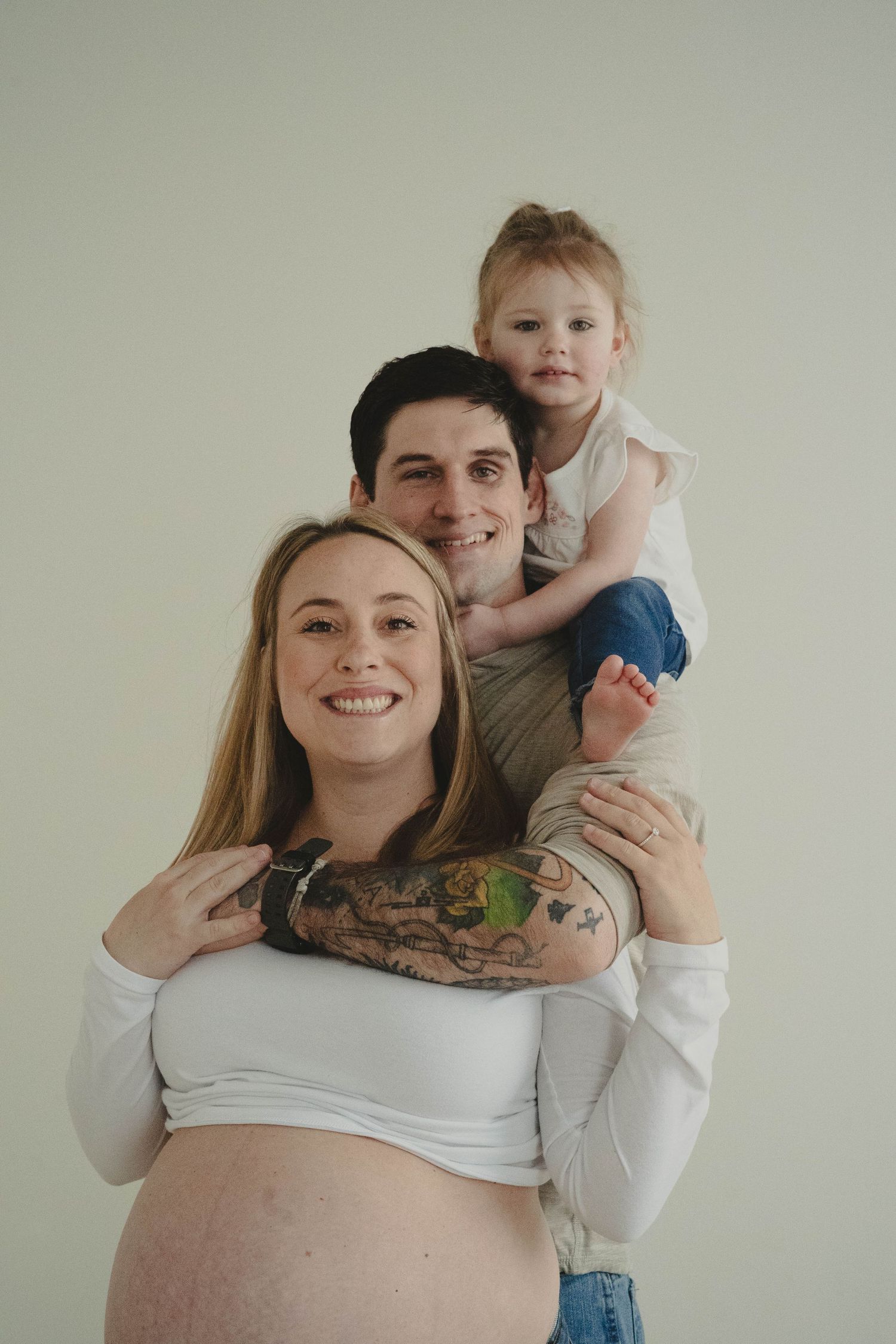 Candid family maternity photos in a bright minimalist studio setting.