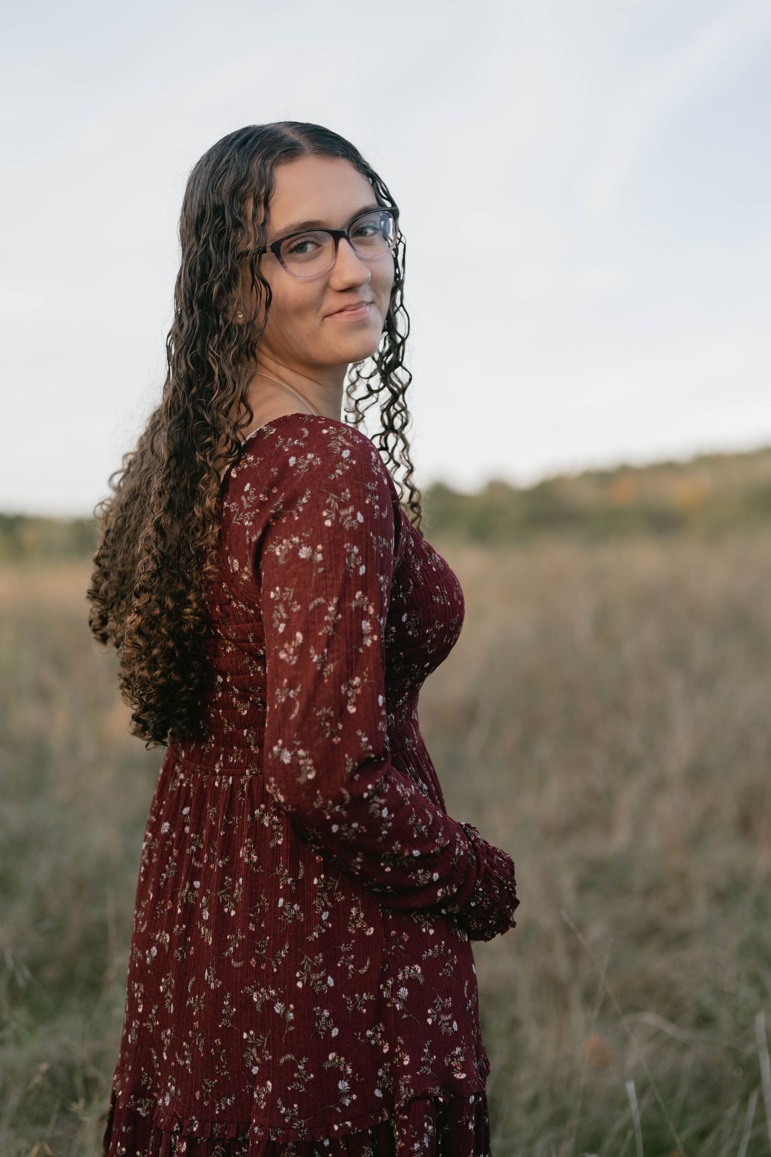 Senior standing in a field of tall grass, smiling and enjoying natural sunlight.