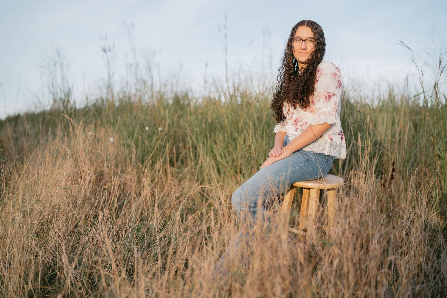 Senior standing in open grassy field at sunset, warm and dreamy portrait.