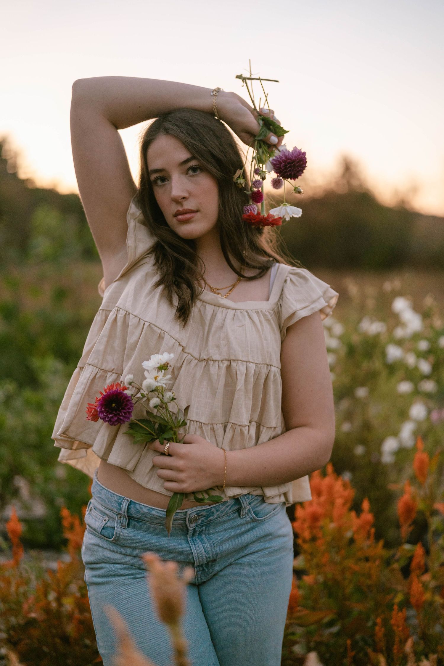 Senior standing among colorful flowers, smiling in a sunlit outdoor portrait.
