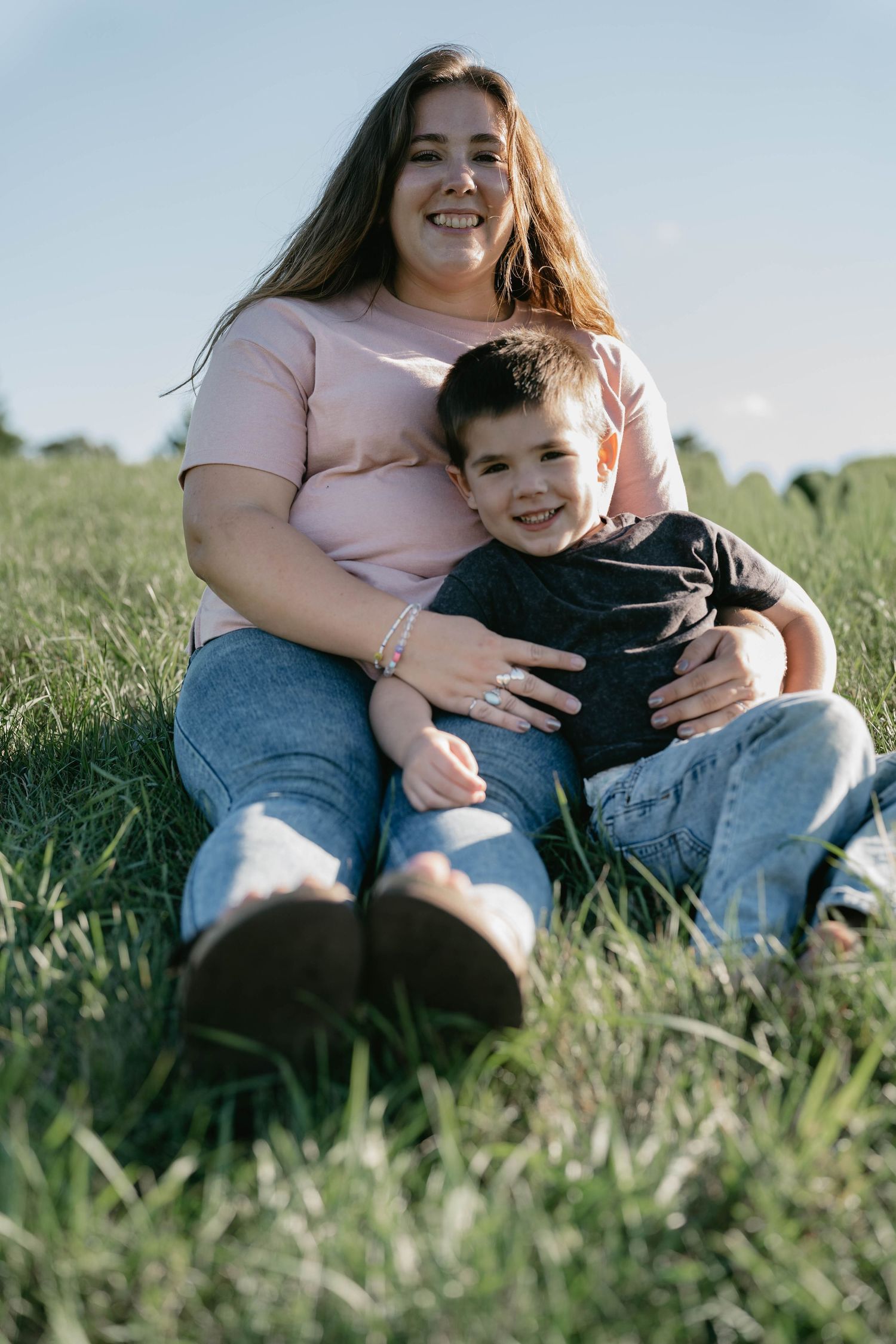 A parent and child share a tender moment sitting together in a grassy meadow on a sunny afternoon.